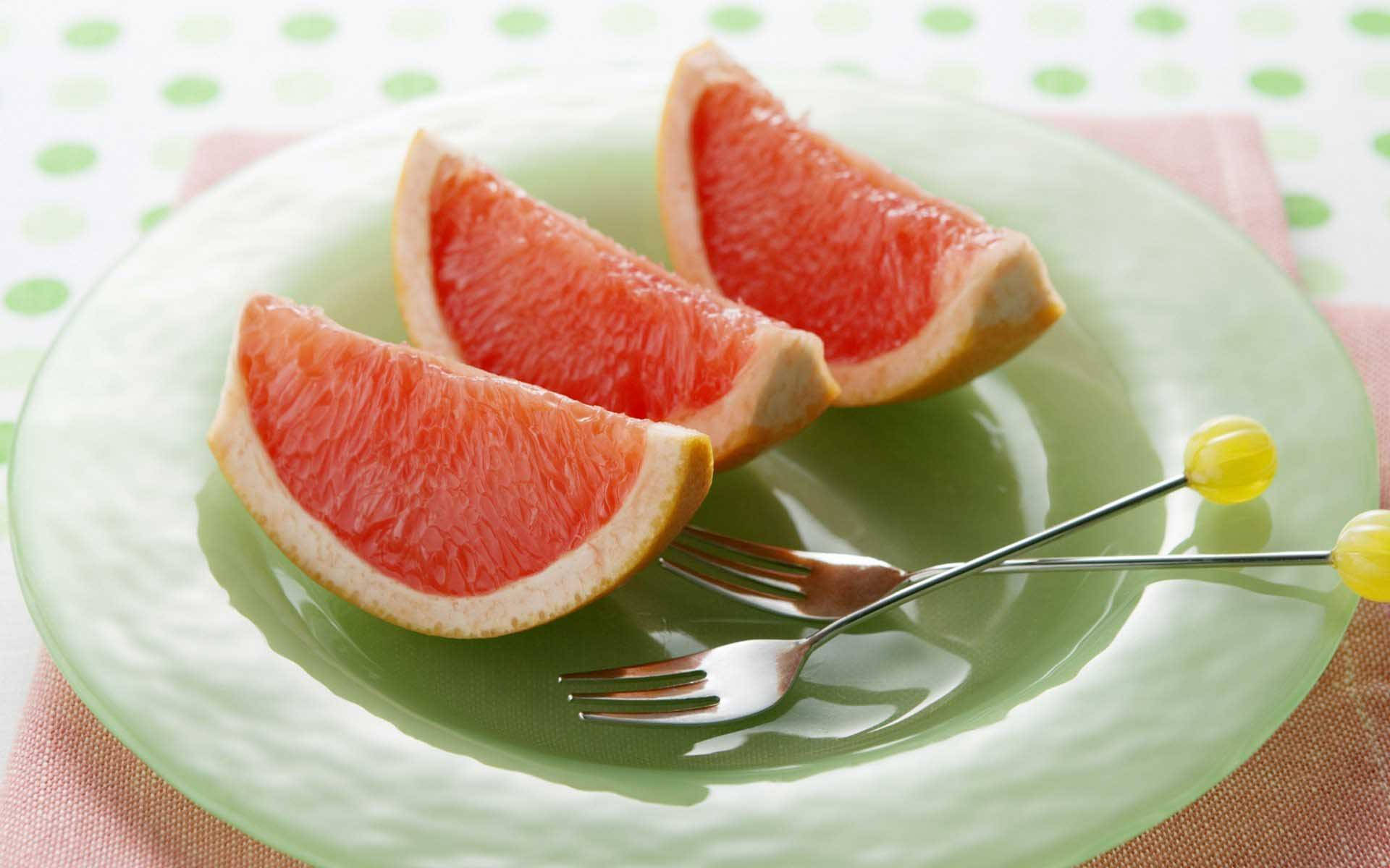 Grapefruit 桌布 壁紙 — 三塊多汁的葡萄柚角放在綠色盤子上，旁邊有兩把叉子，置於圓點桌布上。