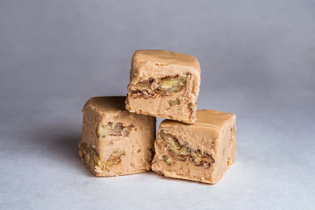 Penuche Fudge 桌布 壁紙 — 三塊奶油色的焦糖軟糖方塊，上面有明顯的胡桃，堆疊在柔軟的灰色表面上。
