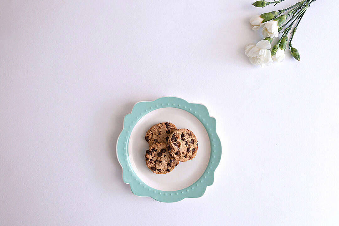 Cookie 桌布 壁紙 — 三塊巧克力餅乾放在一個扇貝形薄荷色盤子上，旁邊有精緻的白花，襯著潔白的背景。