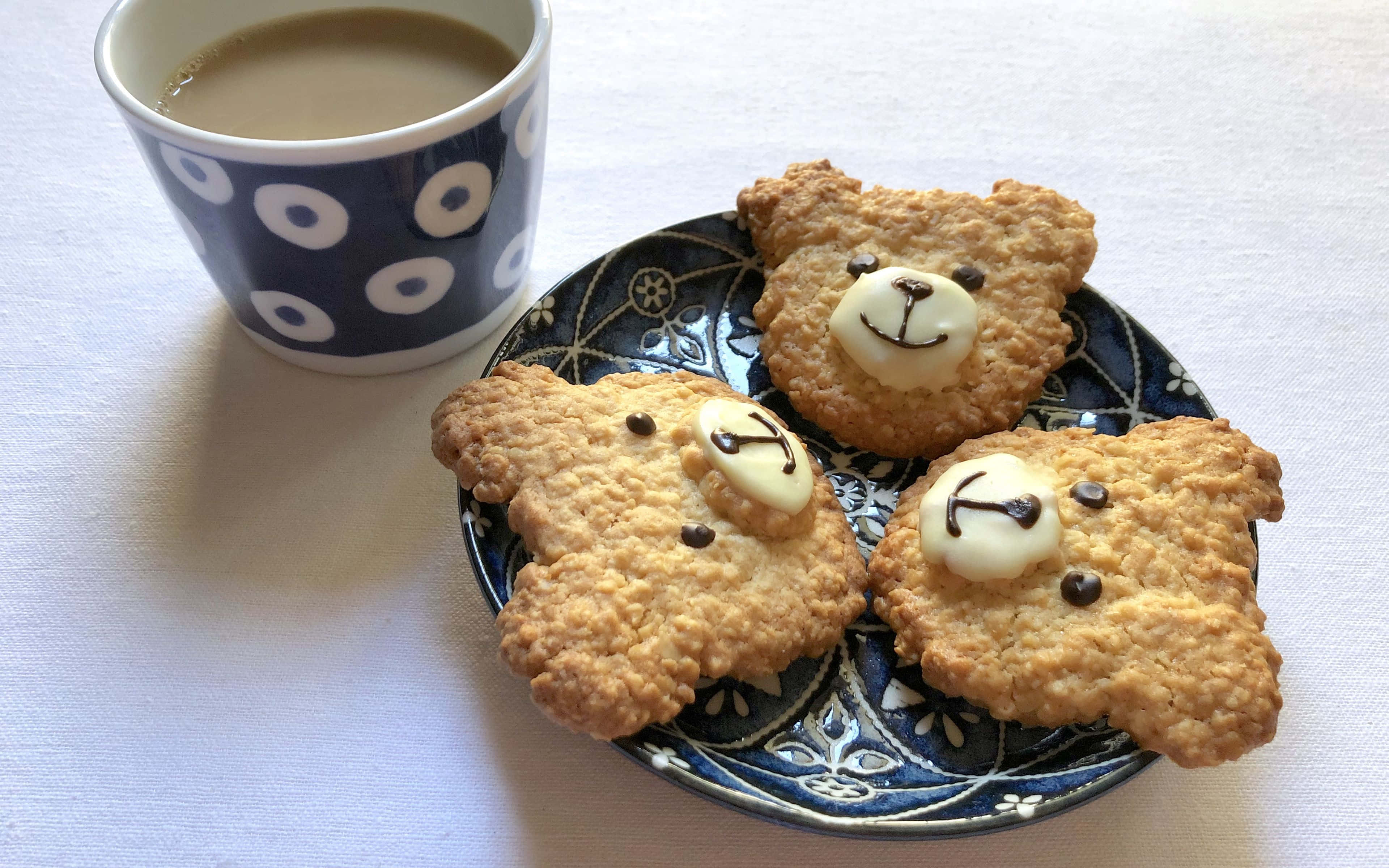 Cookies 桌布 壁紙 — 三塊帶有白色糖霜臉的泰迪熊形狀餅乾，放在一個藍色圖案盤子上，旁邊有一個圓點茶杯。