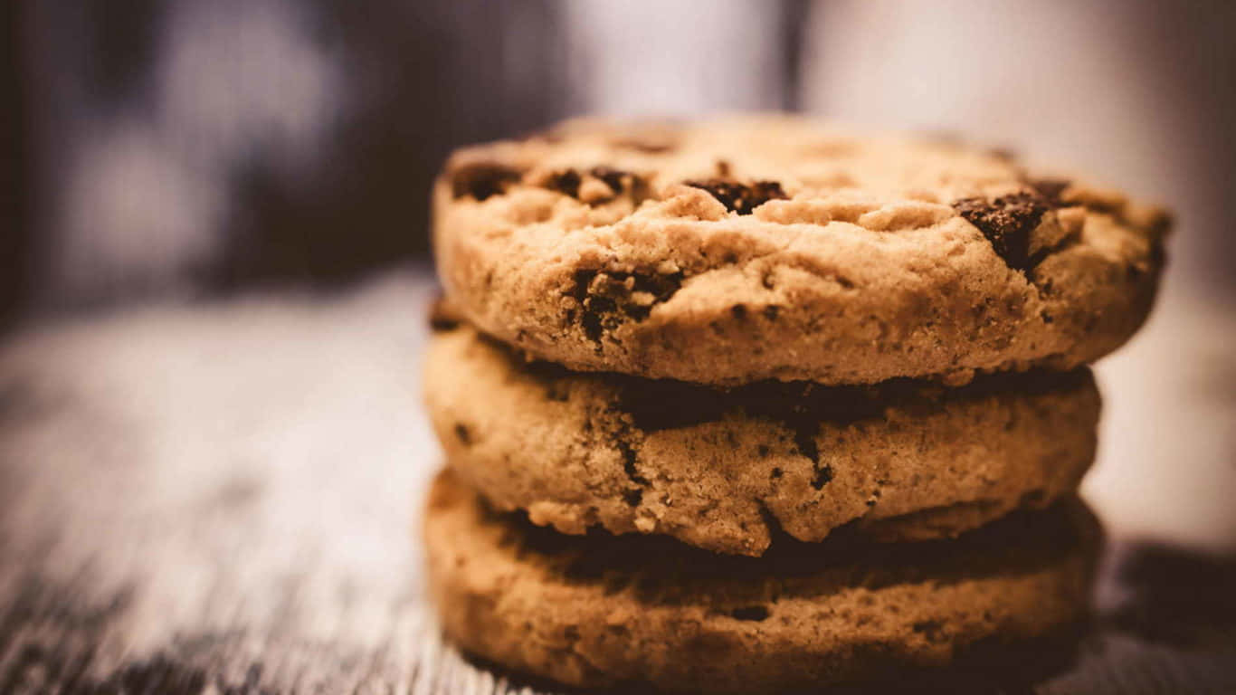 1366x768 Cookies 桌布 壁紙 — 三塊溫暖的巧克力餅乾堆疊在質樸的木質表面上，帶有柔和淺景深效果。