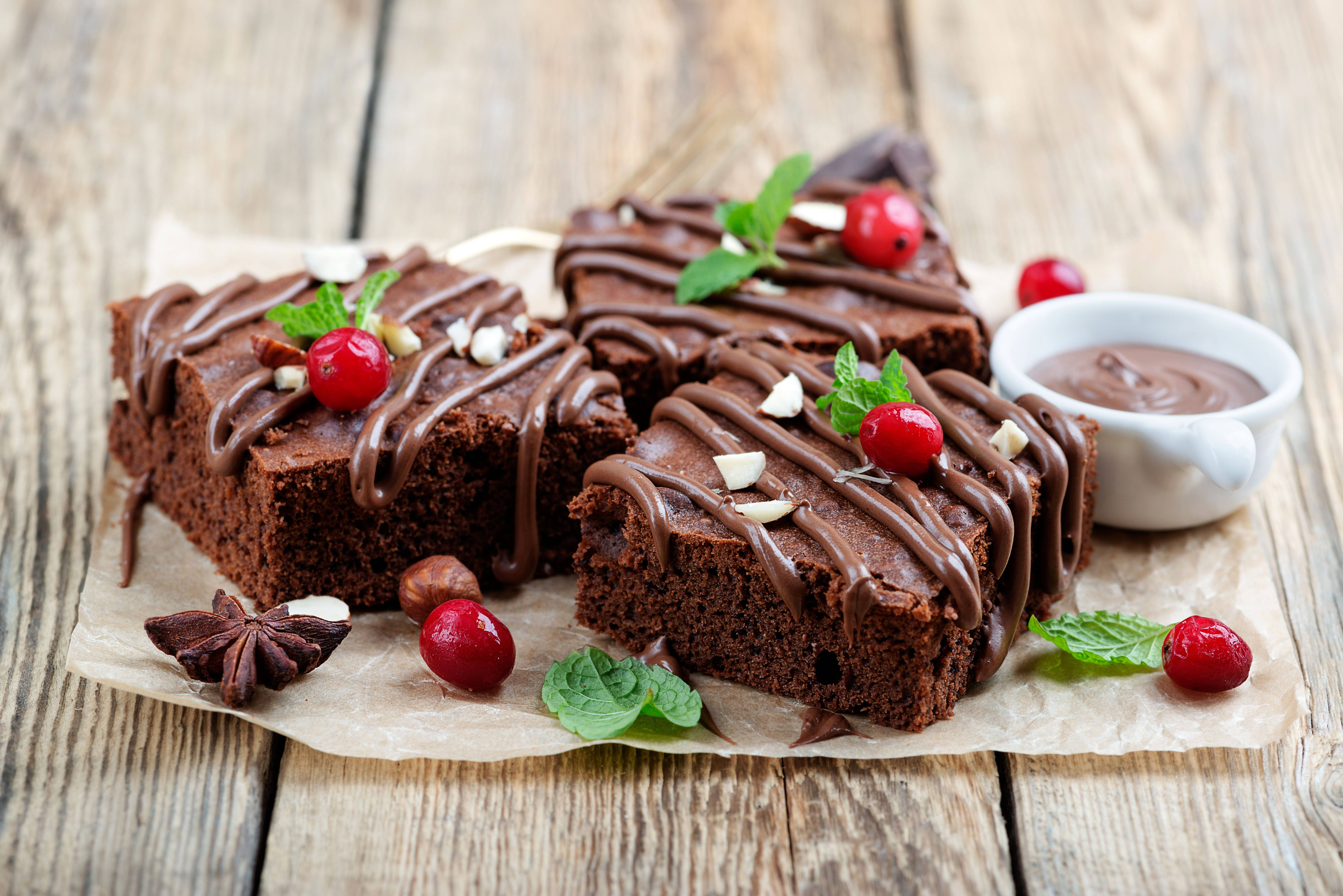 Brownies 桌布 壁紙 — 三塊濃郁的巧克力布朗尼，淋上巧克力醬，飾以蔓越莓和薄荷，放在質樸的木桌上。