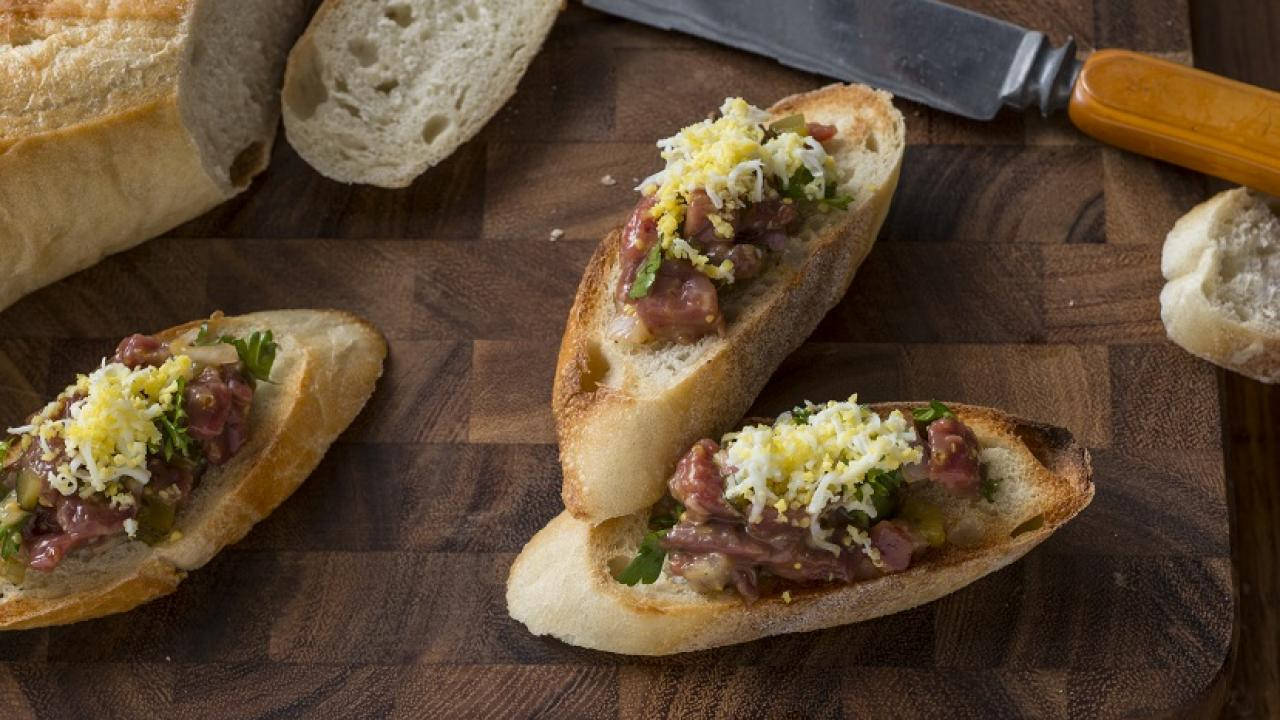 meat 桌布 壁紙 — 三塊烤法國麵包片配上牛肉他他、香草和碎起司，放在木砧板上。