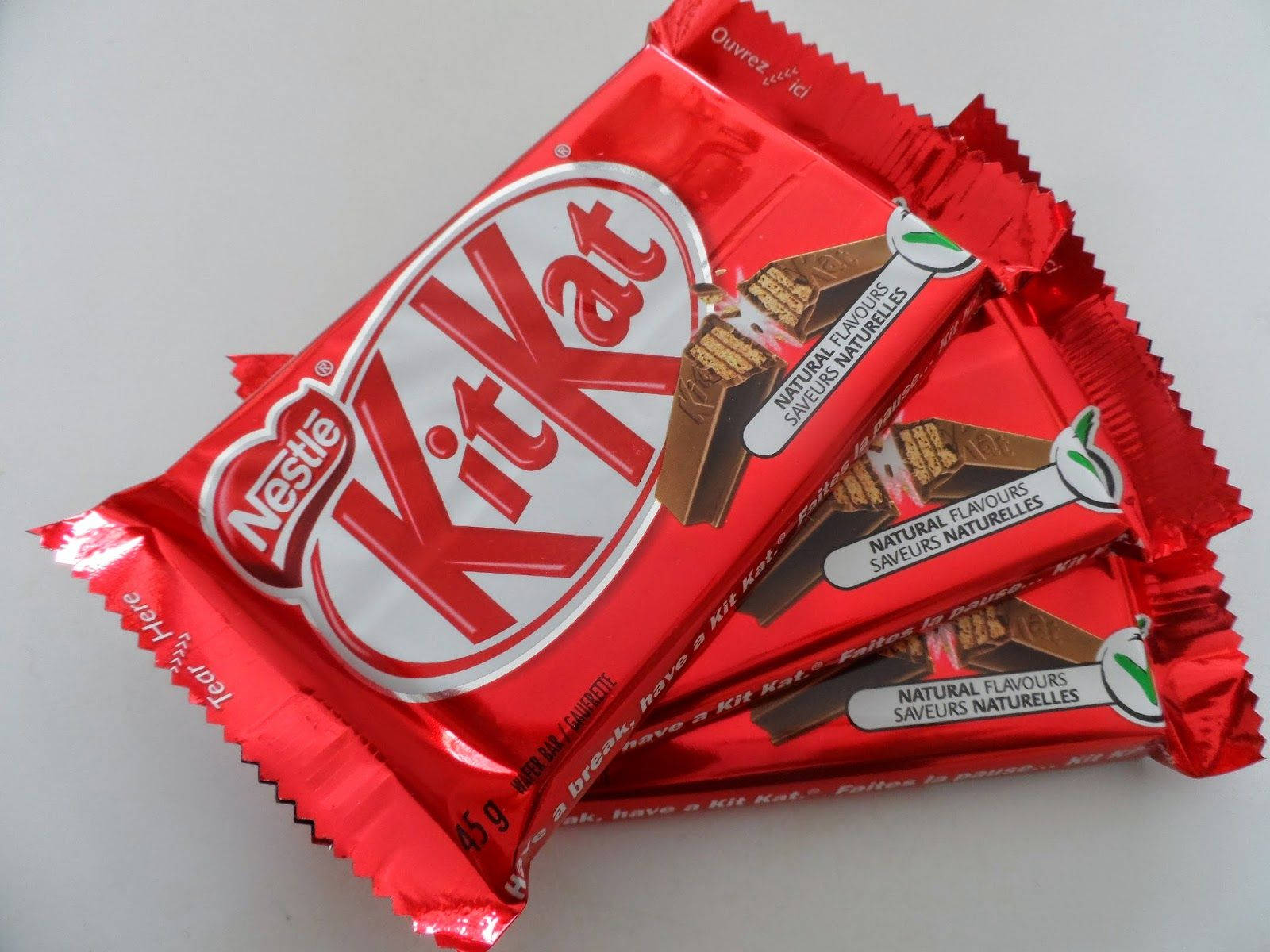 Chocolate 桌布 壁紙 — 三塊紅色錫箔紙包裝的KitKat巧克力棒對角堆疊在純白色表面上。