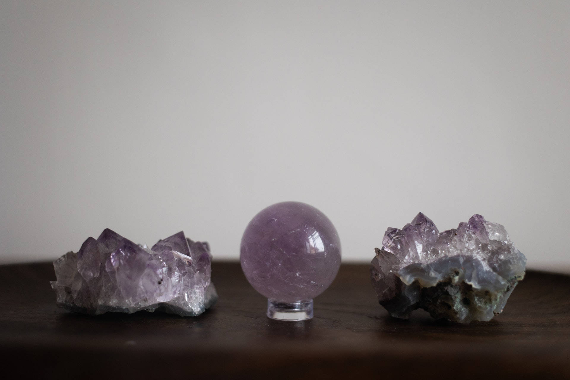 紫水晶 桌布 壁紙 — 三塊紫水晶晶體和一個拋光球體放在深色木質表面上，背景是素牆。