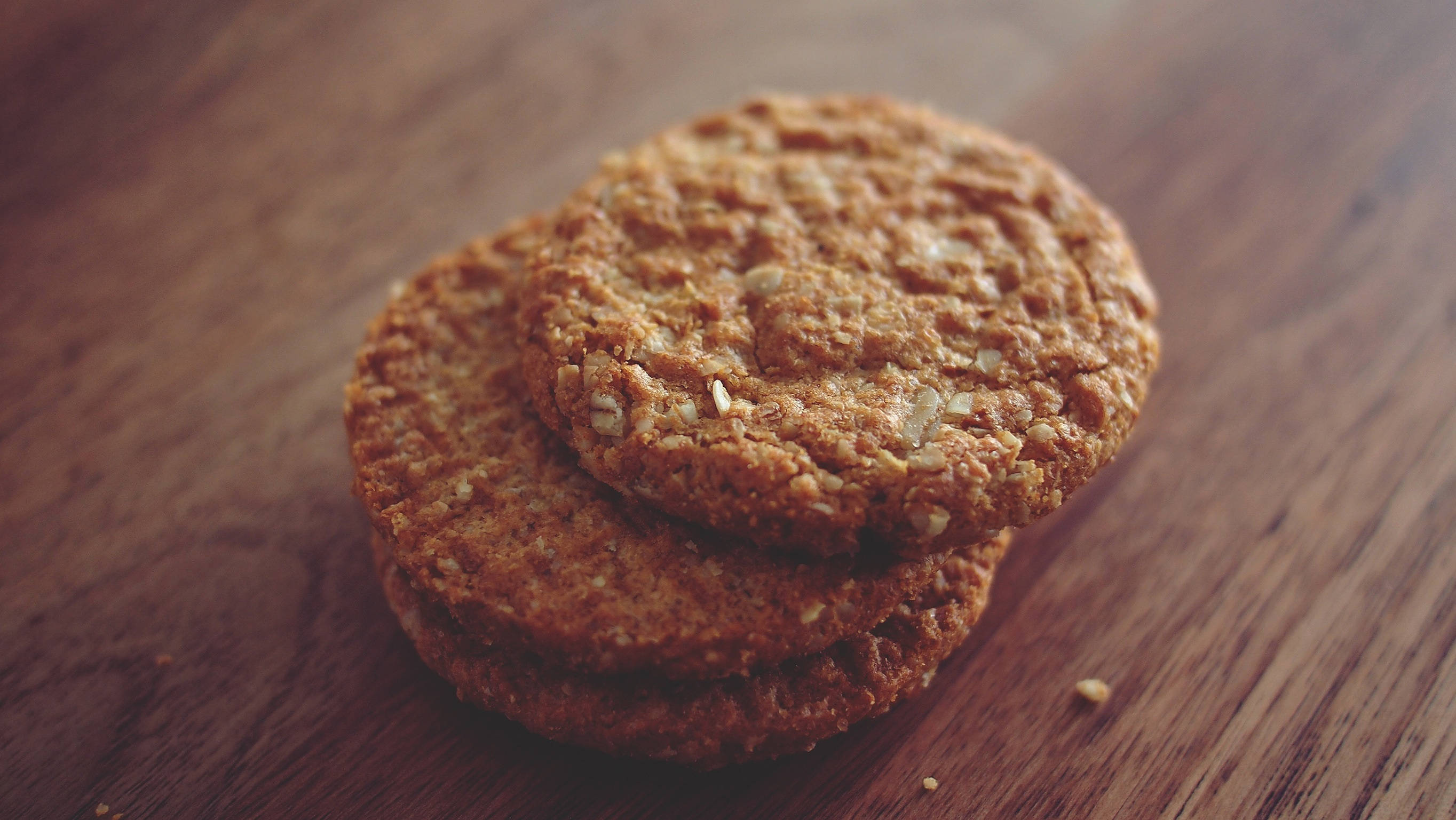 Cookie 桌布 壁紙 — 三塊金黃色的燕麥餅乾堆疊在溫暖的木質表面上，帶有柔和淺景深效果。