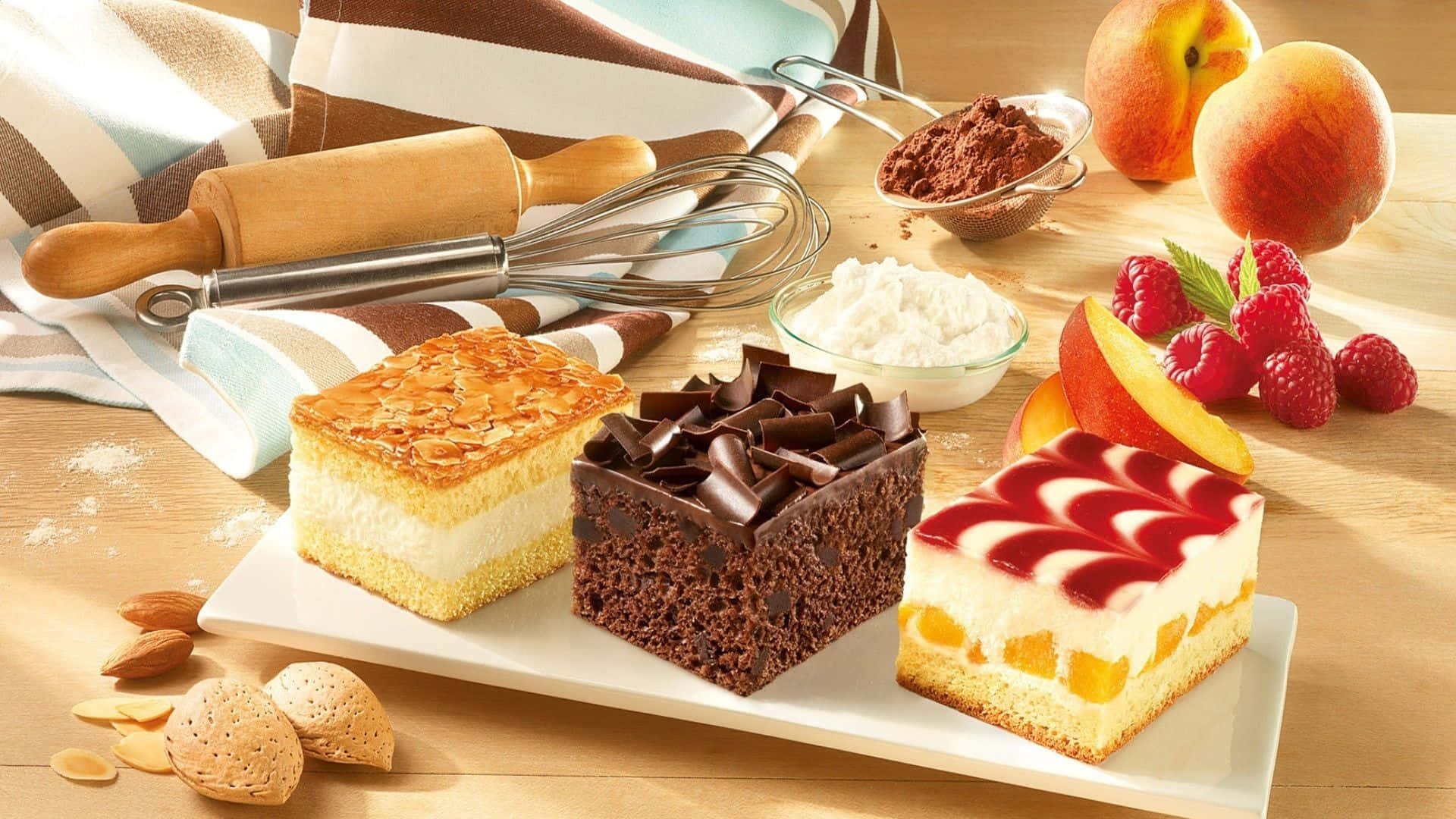Desserts 桌布 壁紙 — 三塊頹廢的甜點方塊，上面有杏仁、巧克力和蜜桃配料，放在木桌上，旁邊有新鮮水果、烘焙工具和糖粉。