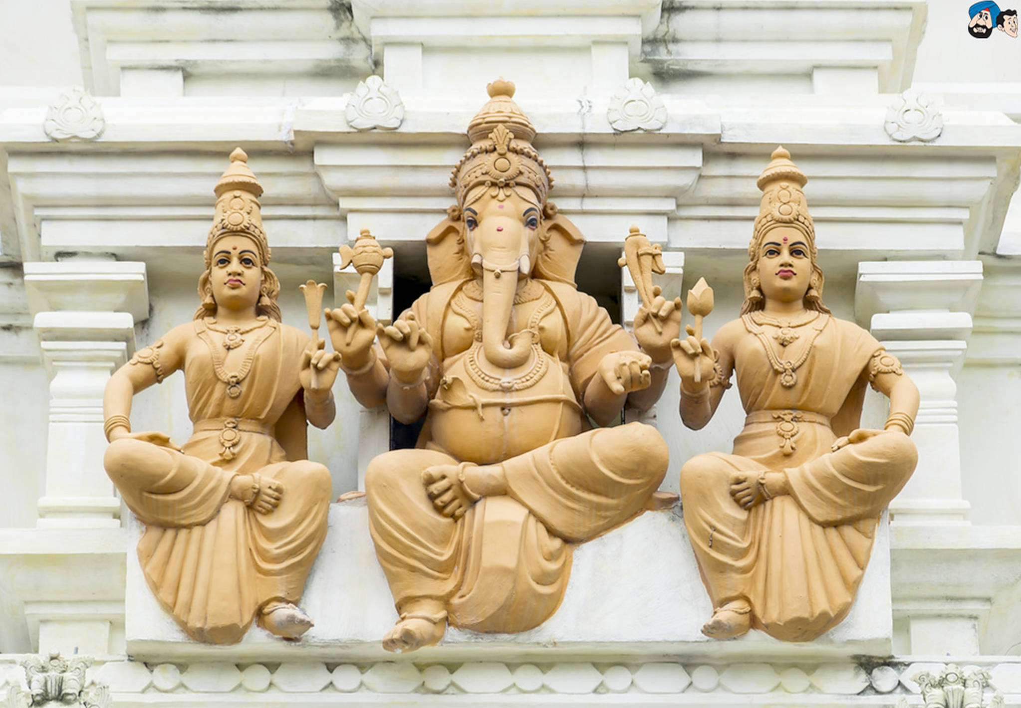 Hindu God 桌布 壁紙 — 三尊棕色的印度教神靈石像，安詳地坐在白色寺廟外牆上，牆上有精緻的雕刻。