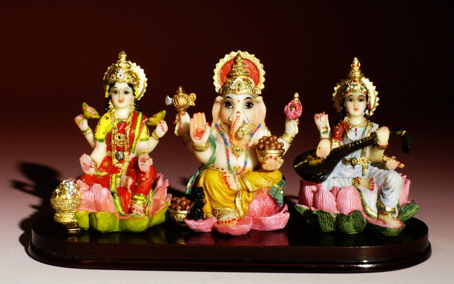 Ganesh 桌布 壁紙 — 三尊色彩繽紛的印度教神像威嚴地坐在蓮花底座上，背景是深紅色。