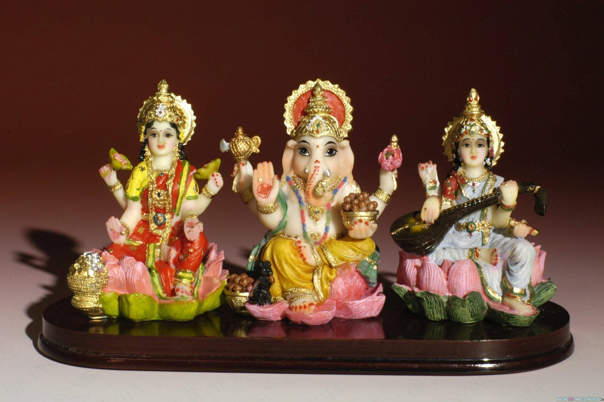 Hindu God 桌布 壁紙 — 三尊色彩繽紛的印度教神像莊嚴地坐在深紅色背景前的深色木架上蓮花座上。