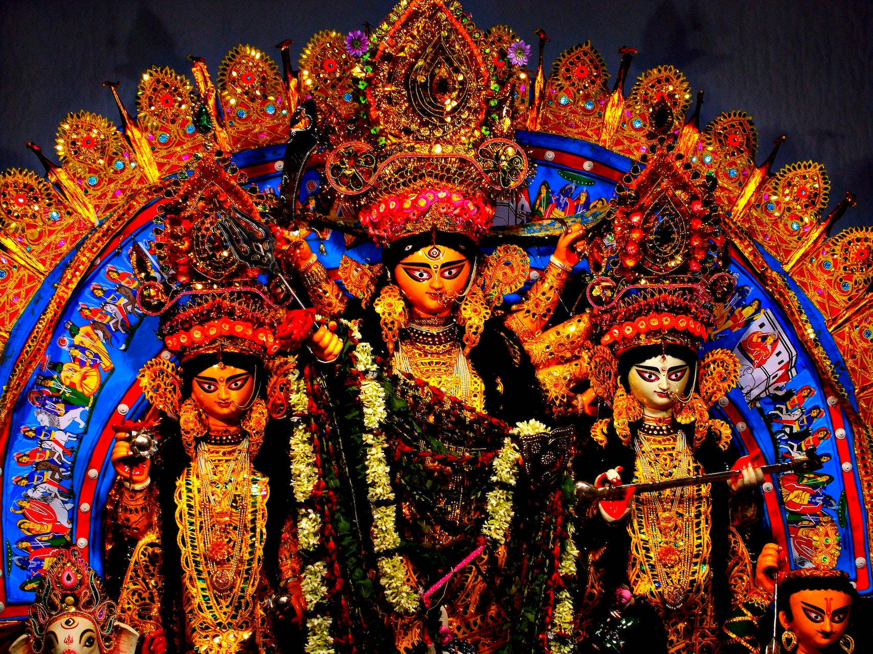 Hindu Temple 桌布 壁紙 — 三尊裝飾精緻的杜爾迦神像，戴著金色皇冠和珠寶，矗立在燦爛的藍金色拱門下。
