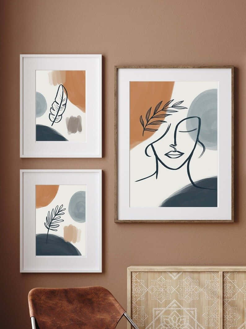 Modern Minimalist Art 桌布 壁紙 — 三幅帶有葉子和面孔極簡線條畫的框裝抽象藝術品，掛在溫暖的棕色牆上，下方是一個有圖案的櫥櫃和皮革椅子。