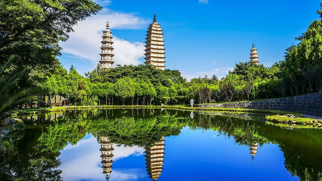 中國 桌布 壁紙 — 三座古塔聳立在茂密的綠樹之上，在晴朗的藍天下完美地倒映在平靜的池塘中。