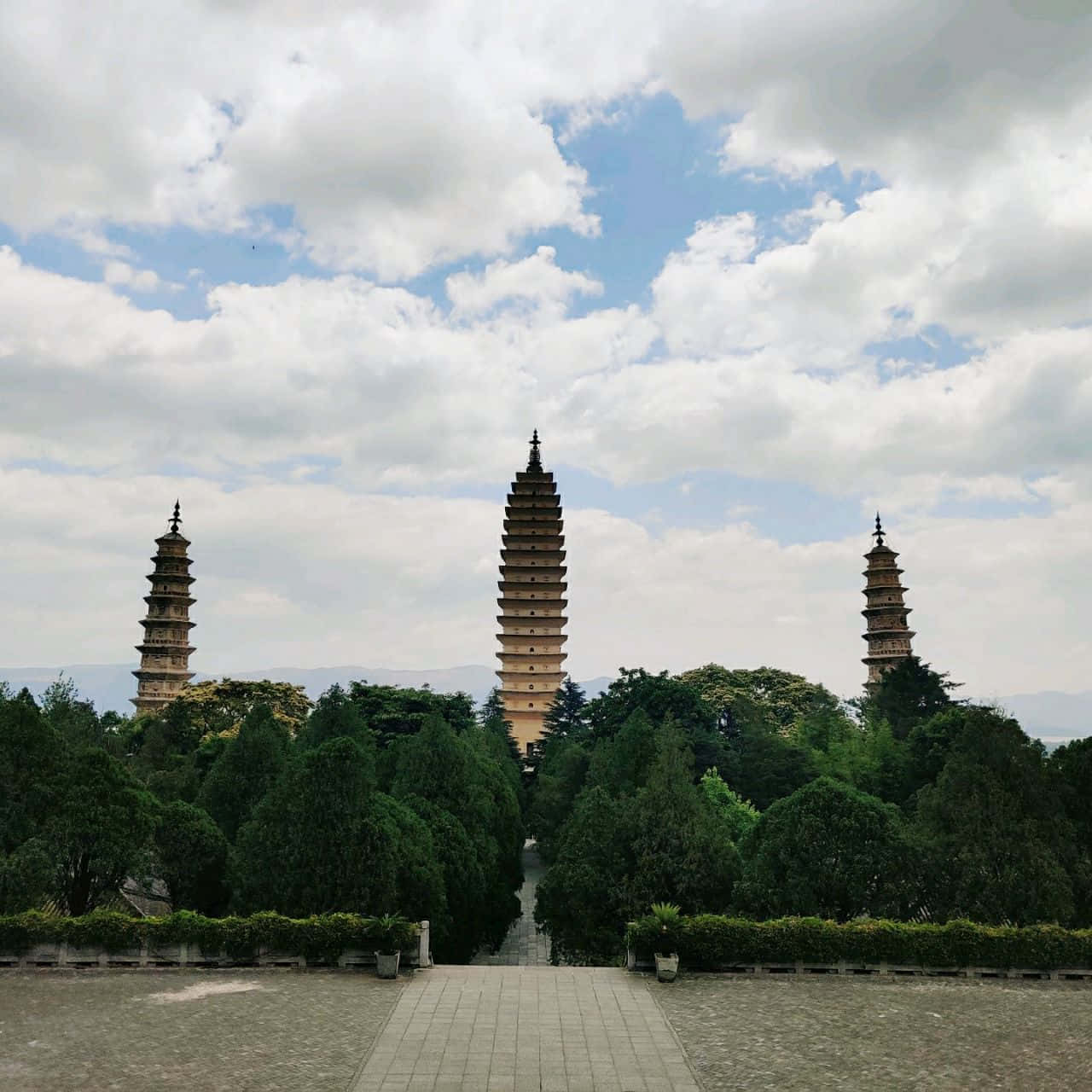 廟宇 桌布 壁紙 — 三座古老石塔聳立在茂密綠樹之上，天空部分多雲，一條鋪砌小徑通向它們。