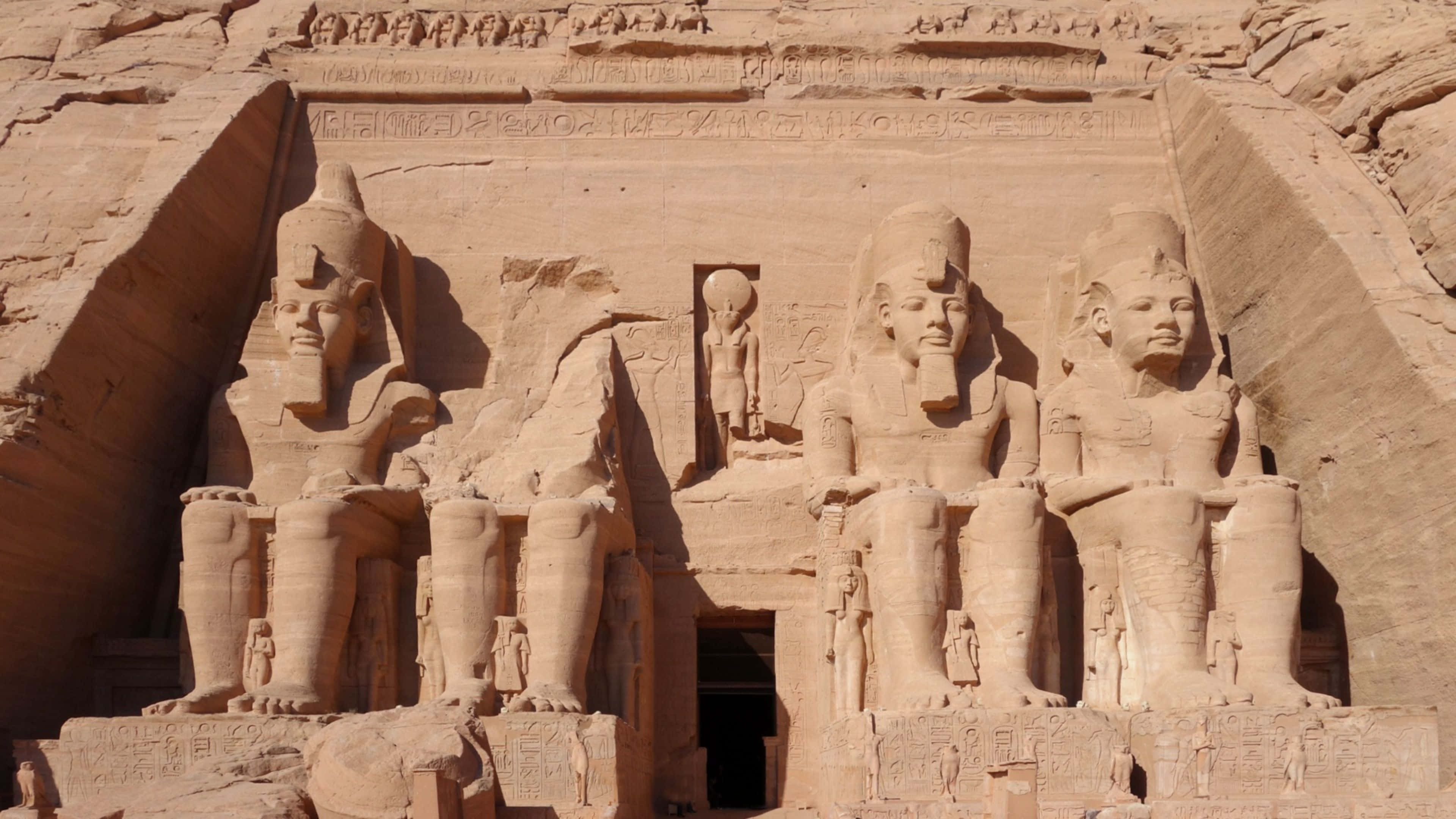 Ancient Egypt 桌布 壁紙 — 三座巨大的坐姿法老雕像雕刻在砂岩懸崖面上，上方有象形文字。