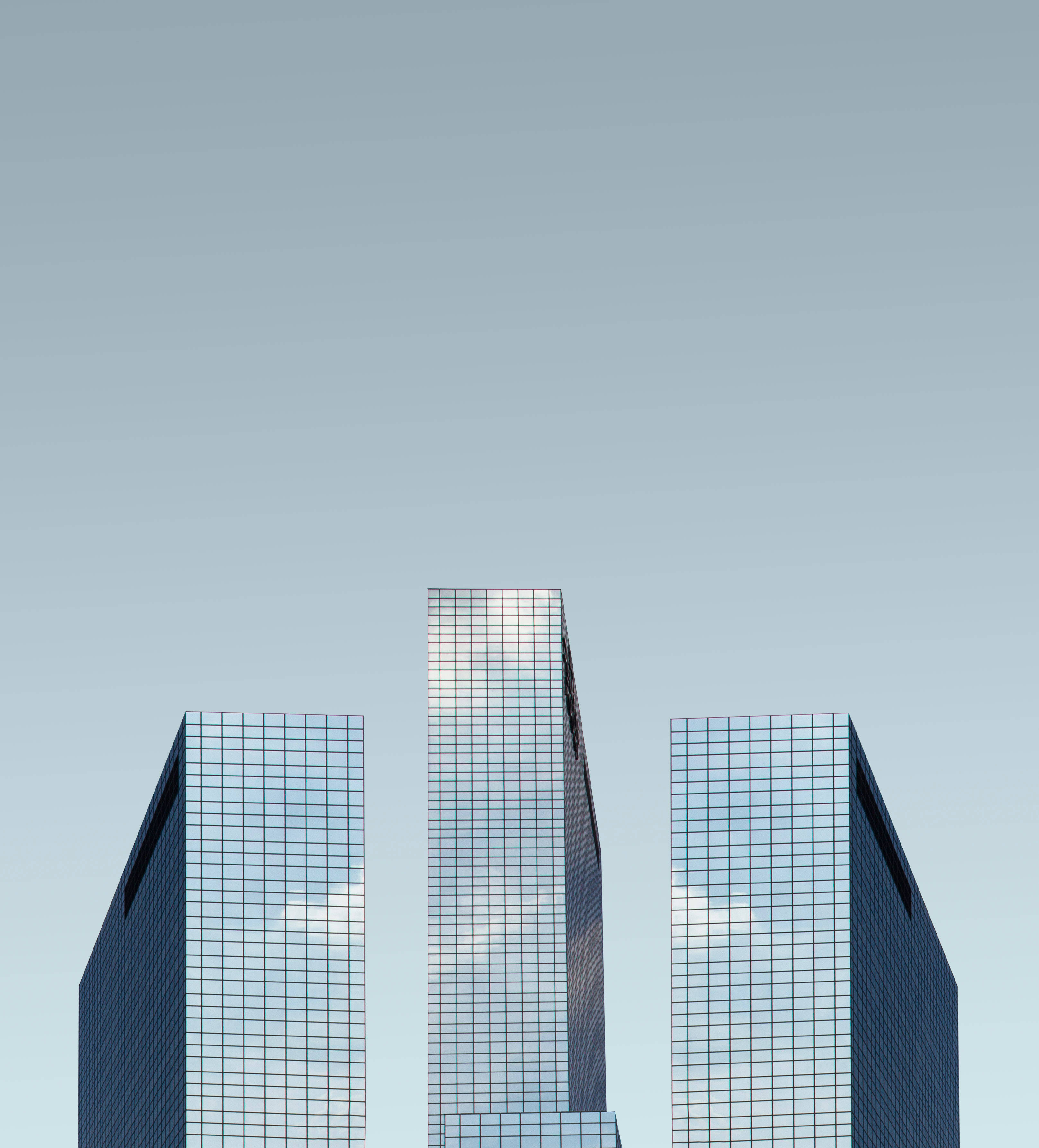 Skyscraper 桌布 壁紙 — 三座玻璃摩天大樓在淡藍色的天空下聳立，將雲朵反射在鏡面外牆上。