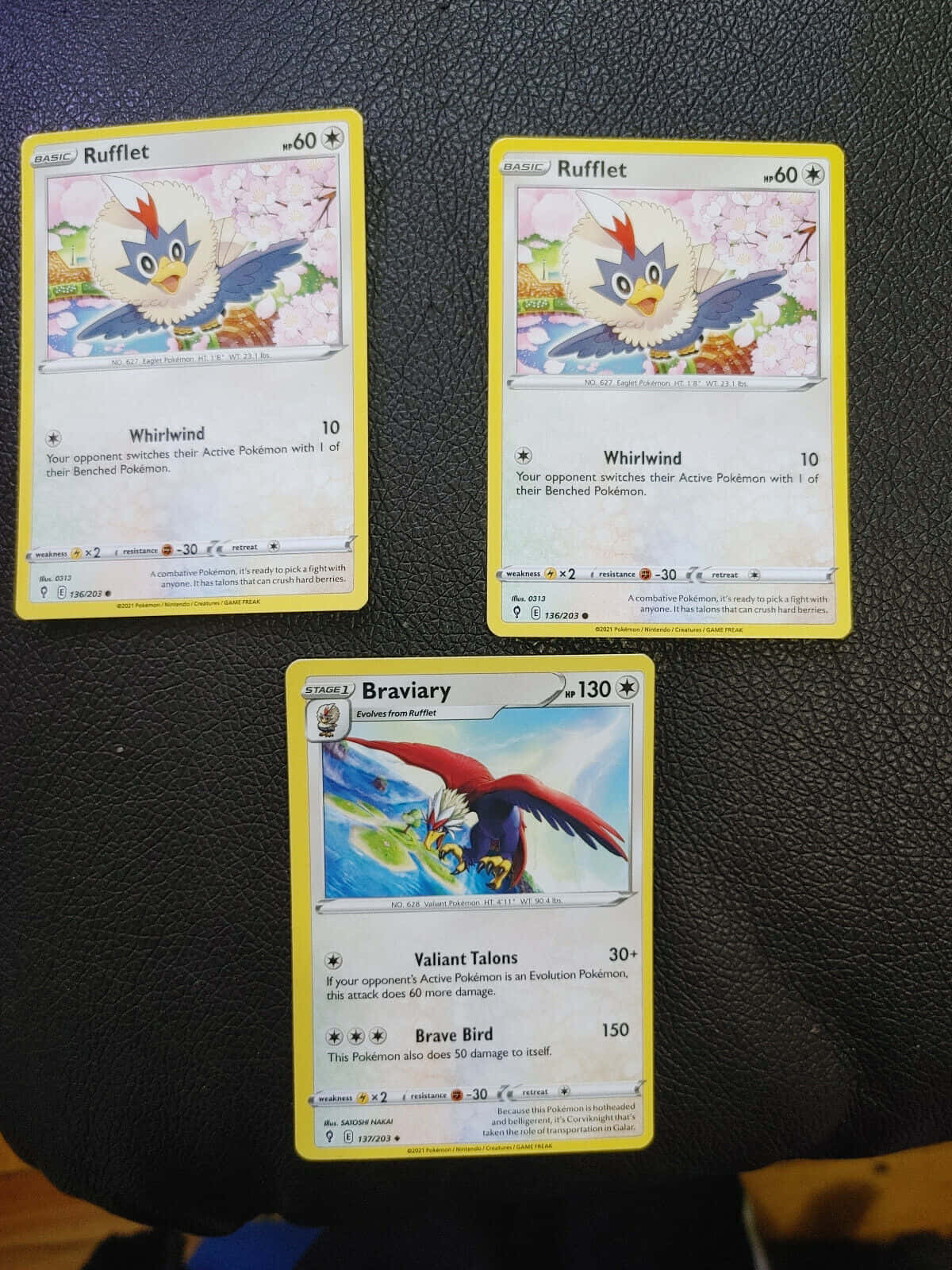 Braviary 桌布 壁紙 — 三張寶可夢集換式卡牌， featuring Rufflet 和 Braviary，置於深色紋理表面上。