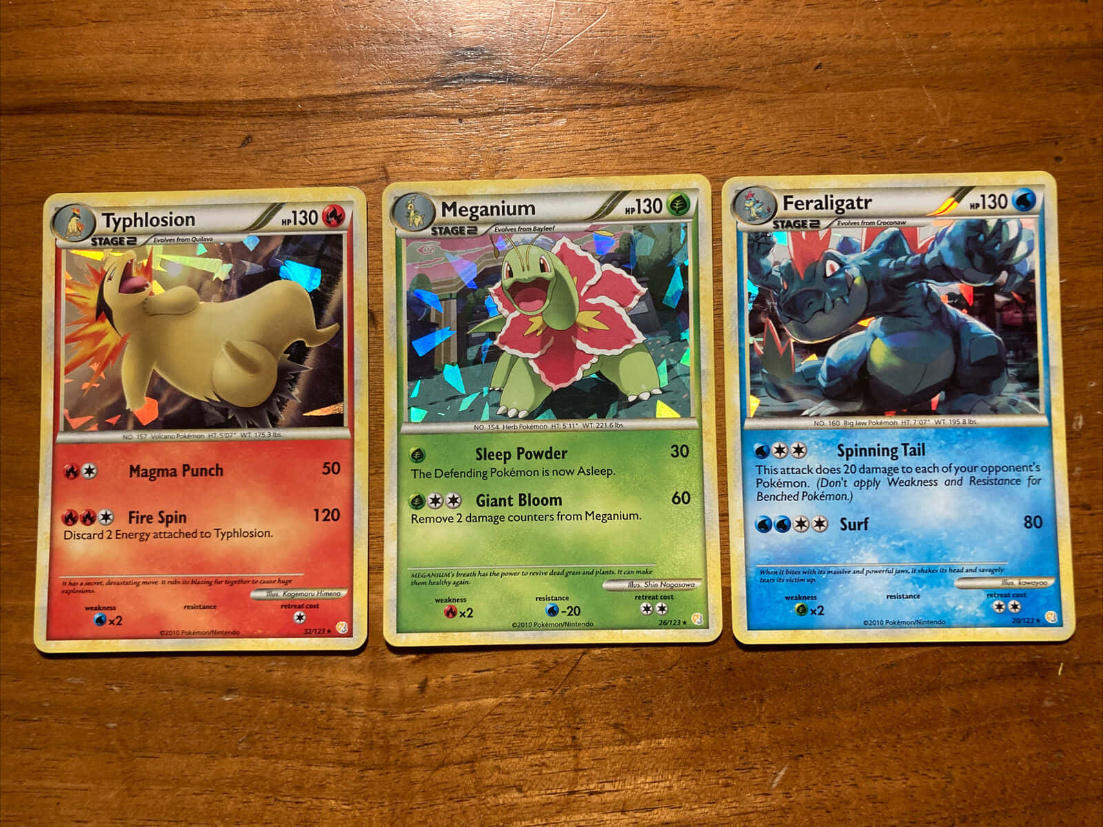 任天堂 桌布 壁紙 — 三張寶可夢集換式卡牌 Typhlosion、Meganium 和 Feraligatr 平放在溫暖的木質表面上。