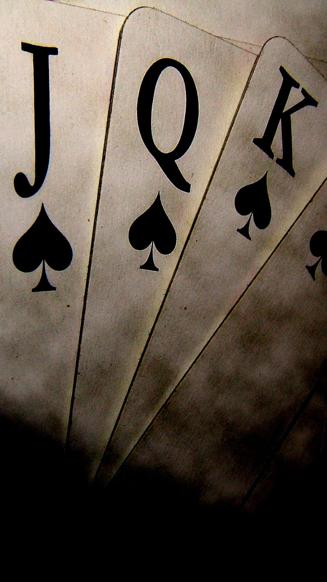 Poker 桌布 壁紙 — 三張復古撲克牌，黑桃J、Q、K，在昏暗光線中展開，帶有戲劇性的陰影。