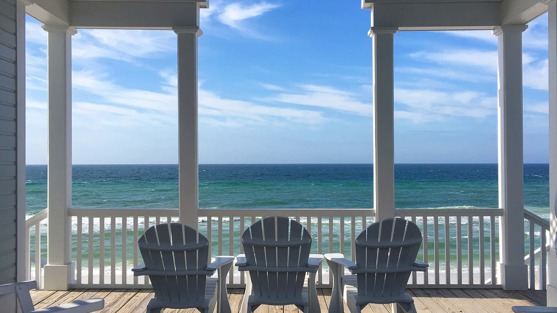 Seaside 桌布 壁紙 — 三張灰色 Adirondack 椅子面向碧綠色的海洋，在明亮的藍天下，從白色柱子的木製門廊上。