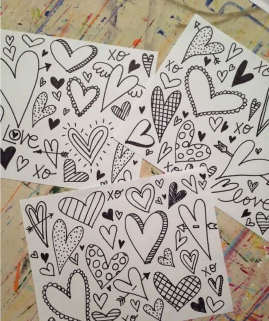 Heart Doodle 桌布 壁紙 — 三張白色紙張上佈滿了手繪的黑色心形圖案，以不同排列方式放在色彩斑斕的顏料濺灑表面上。