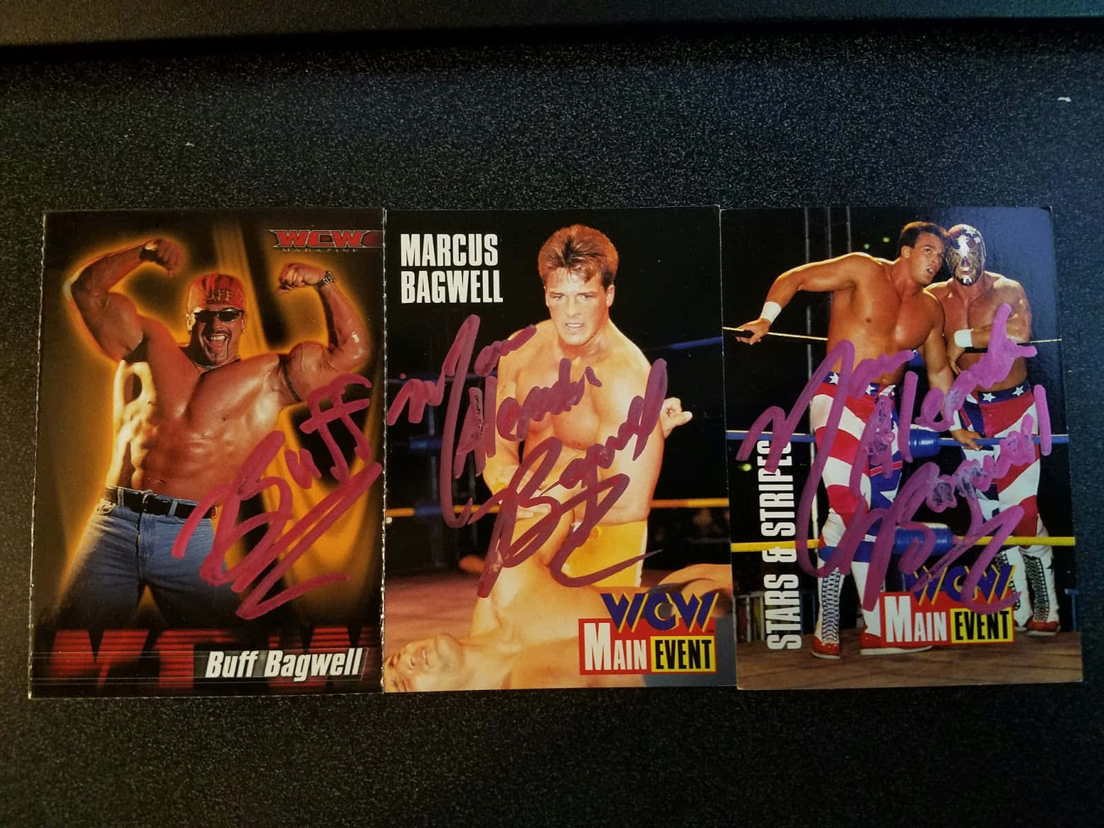 摔角 桌布 壁紙 — 三張簽名WCW摔角交易卡， featuring Buff Bagwell、Marcus Bagwell 和一名蒙面摔角手，置於深色表面上。
