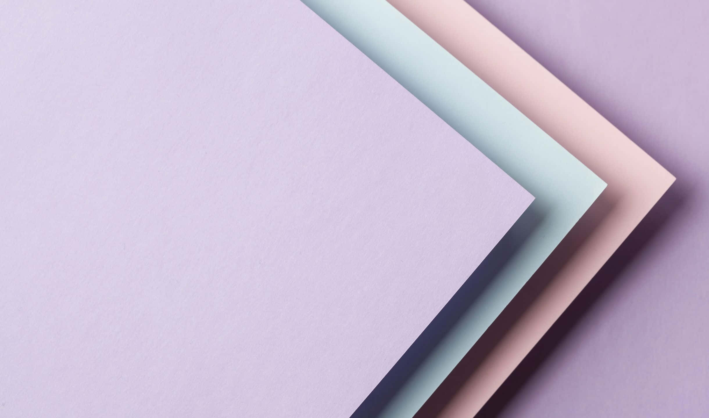 2440x1440 Material 桌布 壁紙 — 三張粉彩色紙張，分別為薰衣草色、薄荷色和腮紅粉紅色，以對角線排列在相配的薰衣草色背景上。