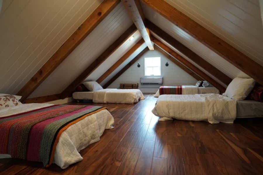cabin 桌布 壁紙 — 三張舒適的床鋪著彩色毯子，放置在一個有木樑拱形天花板的鄉村風格閣樓房間裡，房間內有硬木地板和一扇小窗戶。