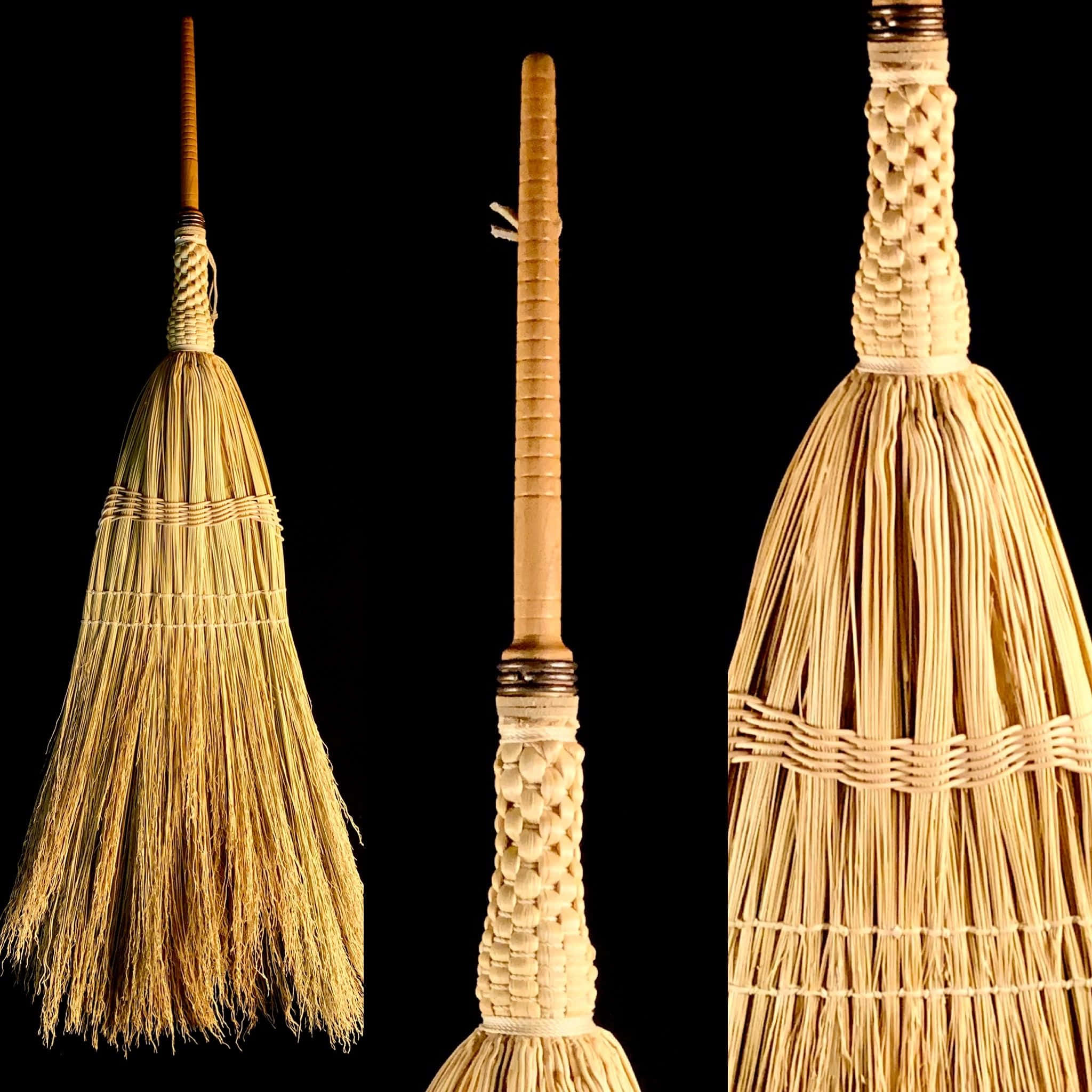 Broom 桌布 壁紙 — 三把傳統稻草掃帚，帶有編織手柄，在純黑背景前展示。
