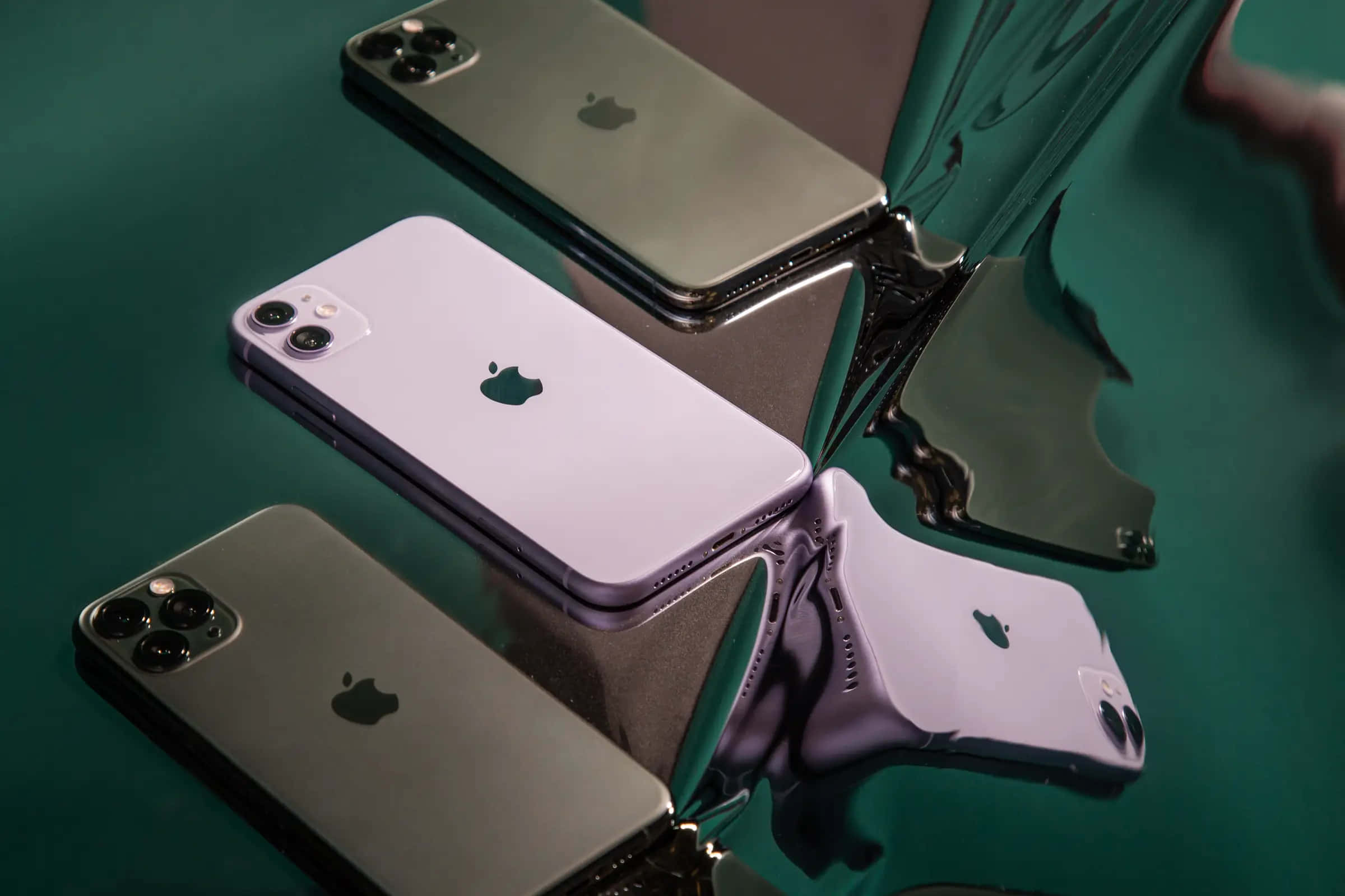 Apple Phone 桌布 壁紙 — 三支 Apple iPhone 分別為銀色、紫色和黑色，放置在帶有扭曲反射的亮綠色表面上。