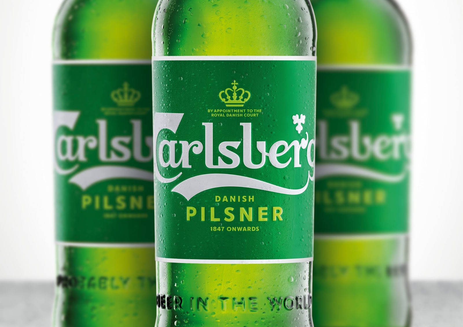 Beer 桌布 壁紙 — 三支冰涼的綠色嘉士伯啤酒瓶帶有冷凝水滴，以淺景深站在明亮的白色背景前。