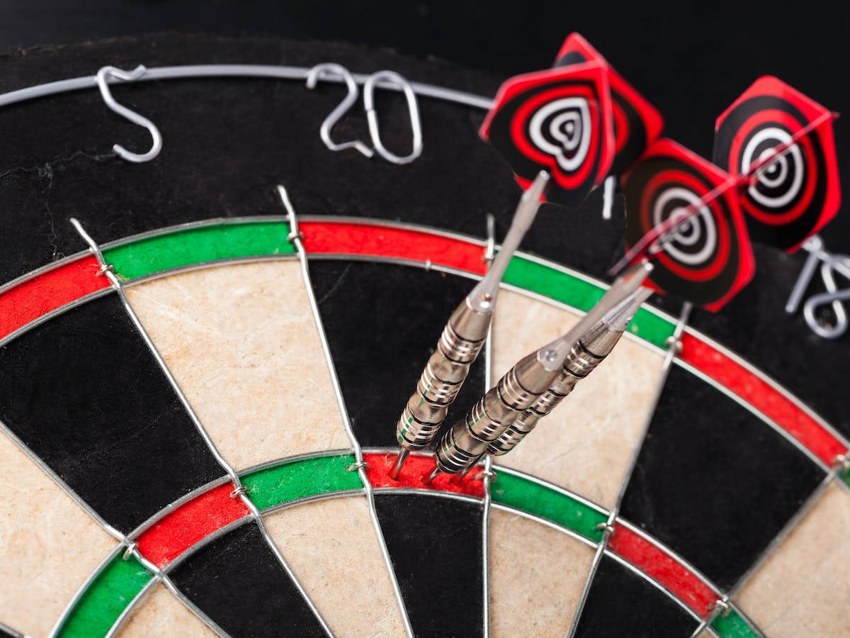 darts 桌布 壁紙 — 三支帶有紅色心形尾翼的飛鏢，在深色背景上刺穿經典飛鏢靶的靶心。