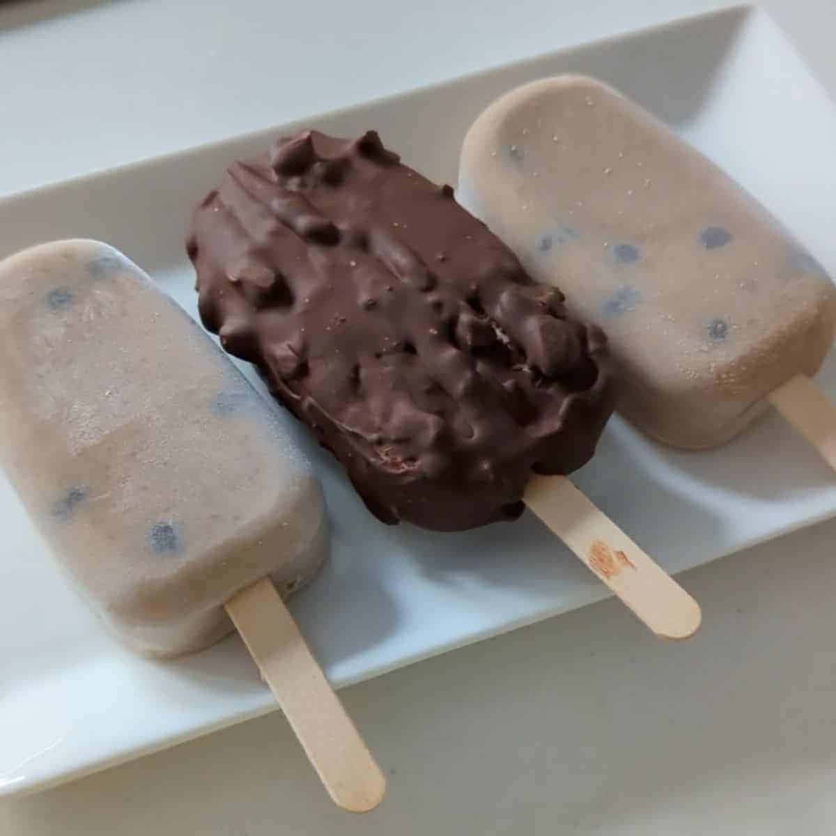 Ice Cream 桌布 壁紙 — 三支帶有藍莓漩渦的奶油冰棒和一支沾有巧克力的冰棒放在白色盤子上。