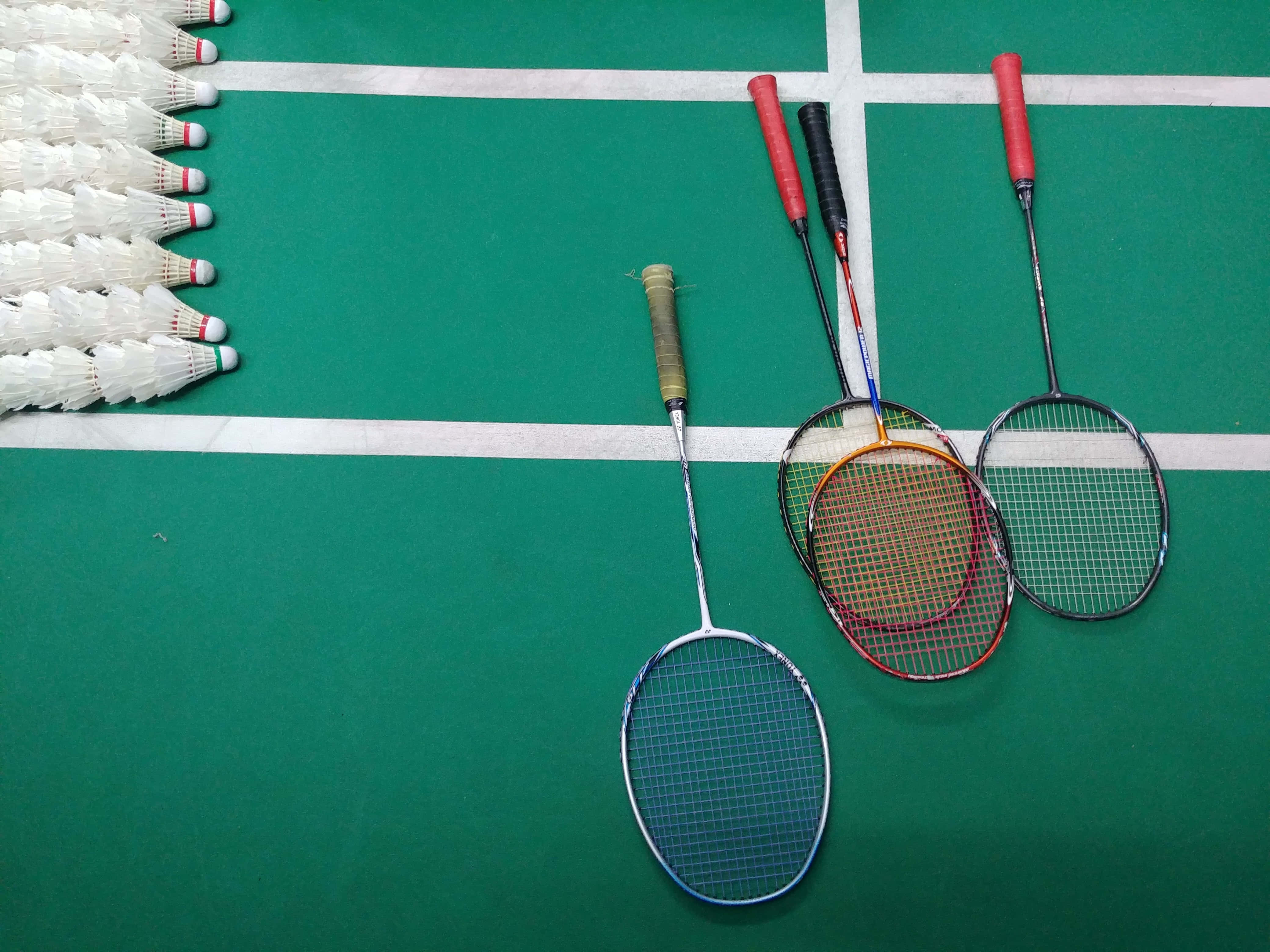 Badminton 桌布 壁紙 — 三支羽毛球拍和一堆羽毛球放在一個有白線標記的綠色球場上。