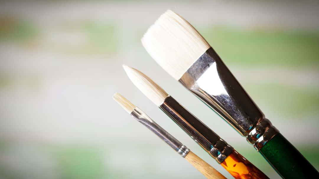Paint Brush 桌布 壁紙 — 三支藝術家畫筆，刷毛和手柄各異，靠在柔和的模糊綠色和白色背景上。