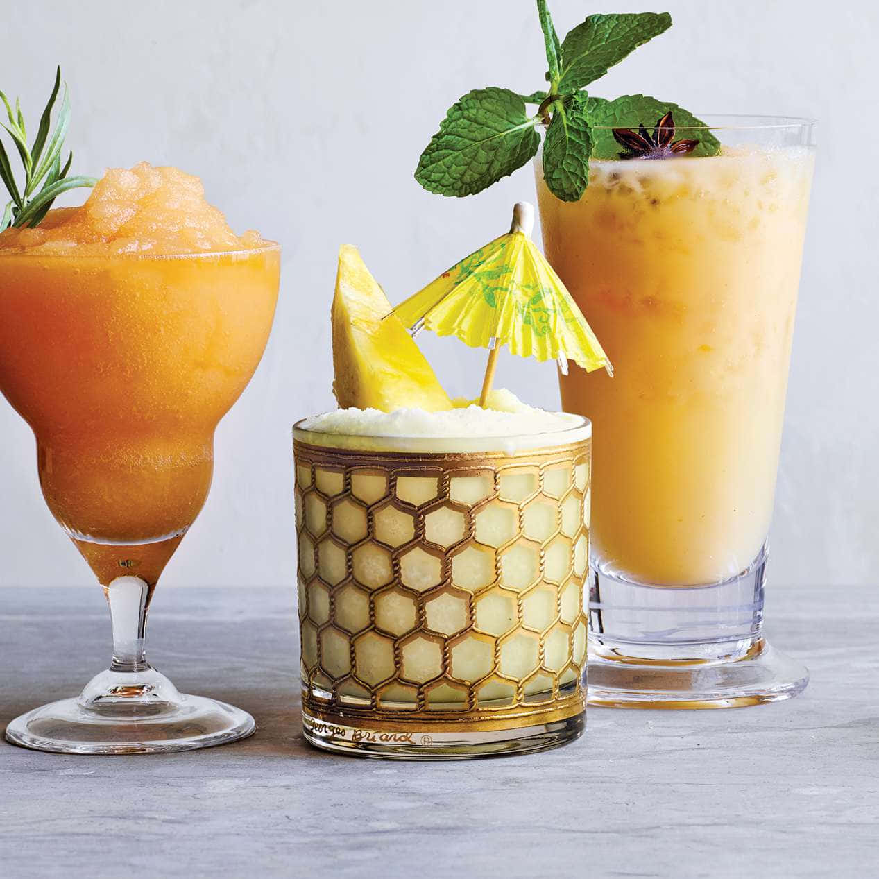 Beautiful Drink 桌布 壁紙 — 三杯充滿活力的熱帶雞尾酒，飾以薄荷、鳳梨和迷迭香，放在灰色表面上。