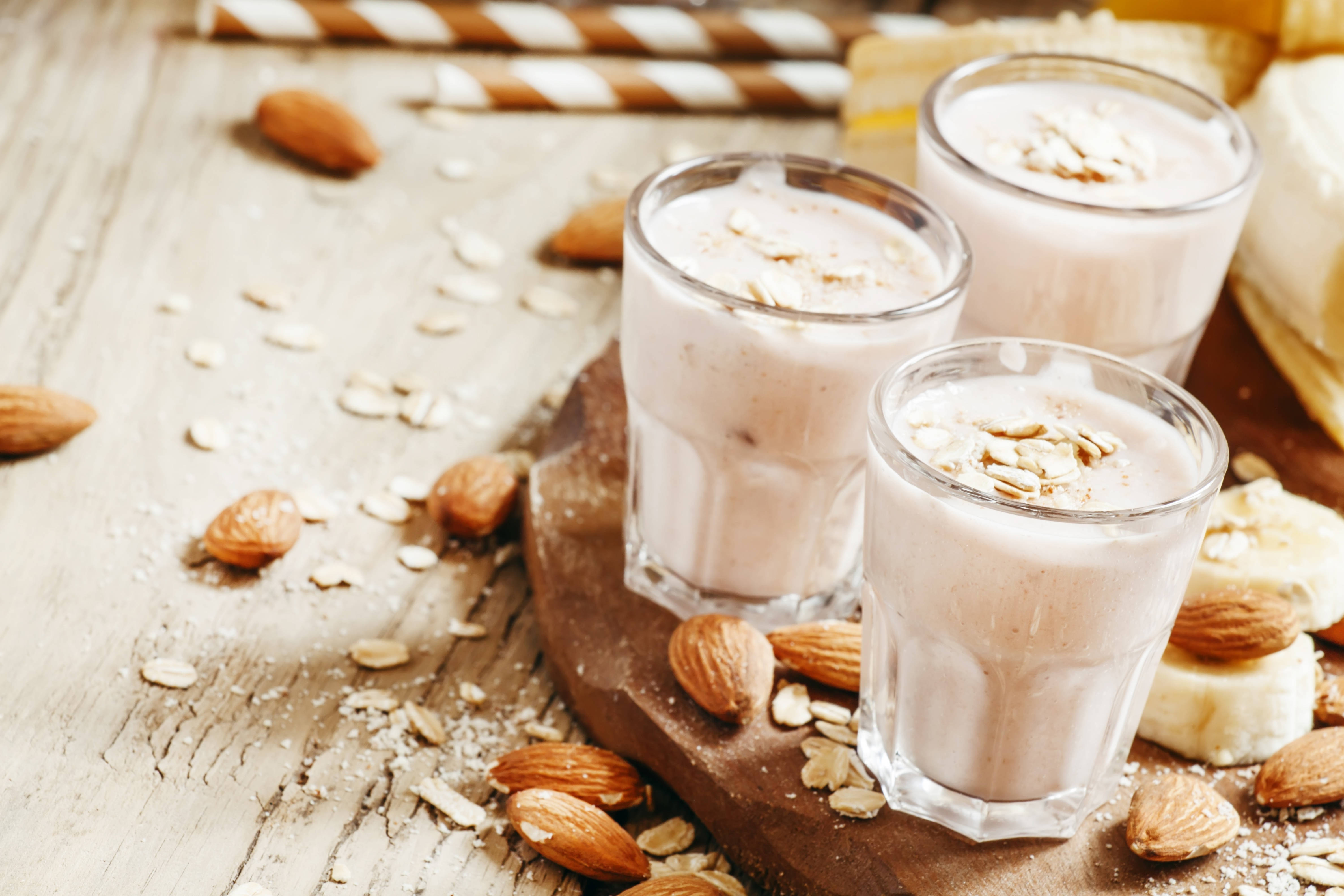 Almond 桌布 壁紙 — 三杯奶油杏仁燕麥奶昔，上面撒上燕麥和杏仁，放在質樸的木板上。
