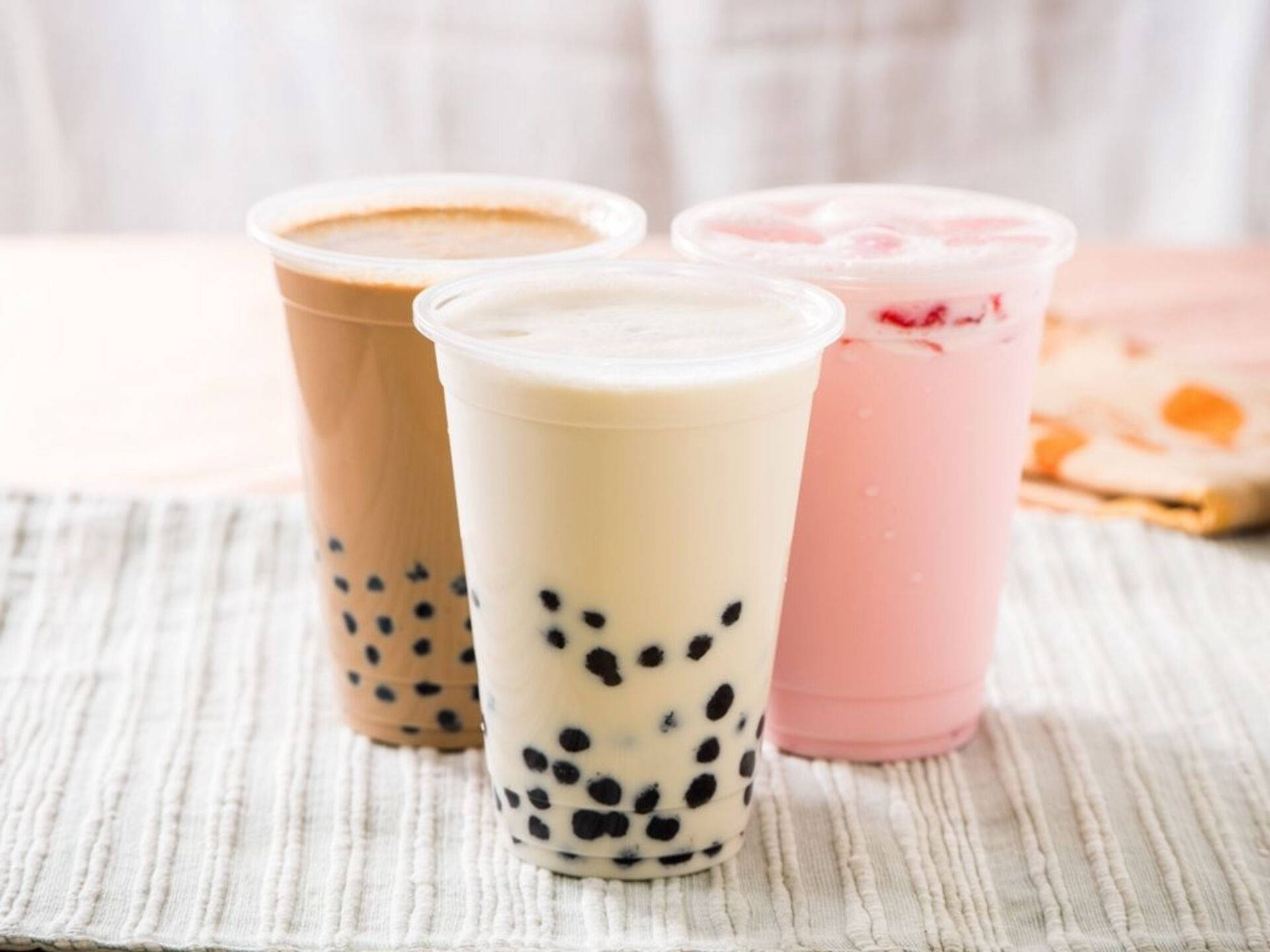 Bubble 桌布 壁紙 — 三杯色彩繽紛的珍珠奶茶放在有紋理的白色墊子上，背景柔和模糊。