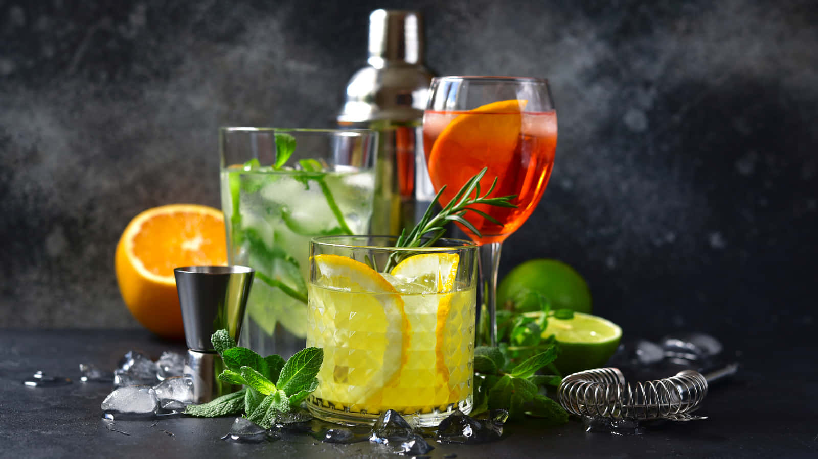alcohol 桌布 壁紙 — 三杯色彩繽紛的雞尾酒，飾以柑橘和香草，置於深色石板表面上，周圍環繞著新鮮水果和酒吧工具。