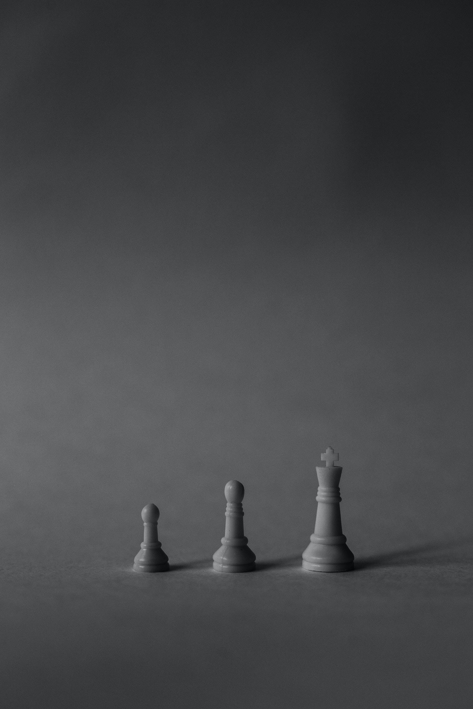 灰色 桌布 壁紙 — 三枚極簡風格的西洋棋棋子，在柔和的灰色漸層背景上以遞增尺寸升起。