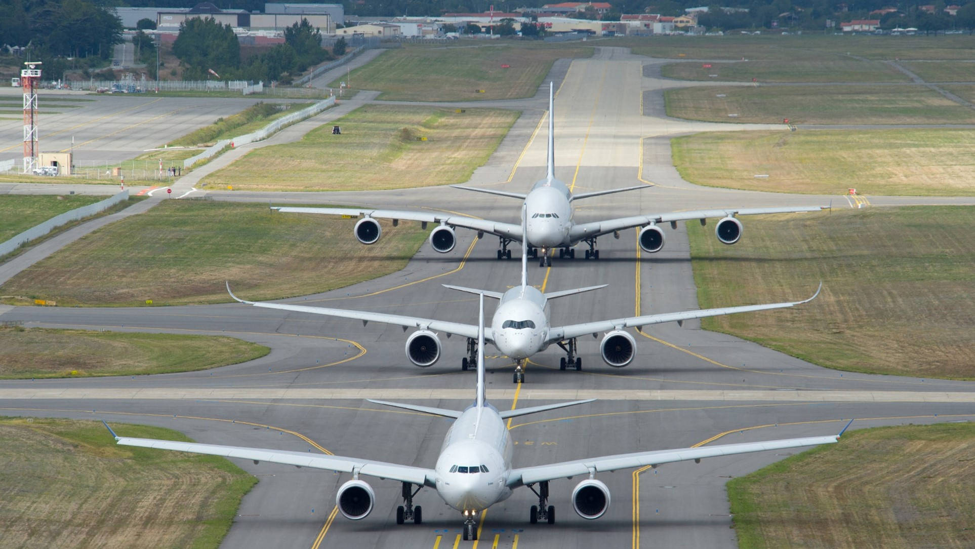 Runway 桌布 壁紙 — 三架大型白色客機在晴朗日光下排列在機場跑道上，周圍有草地和遠處建築物。