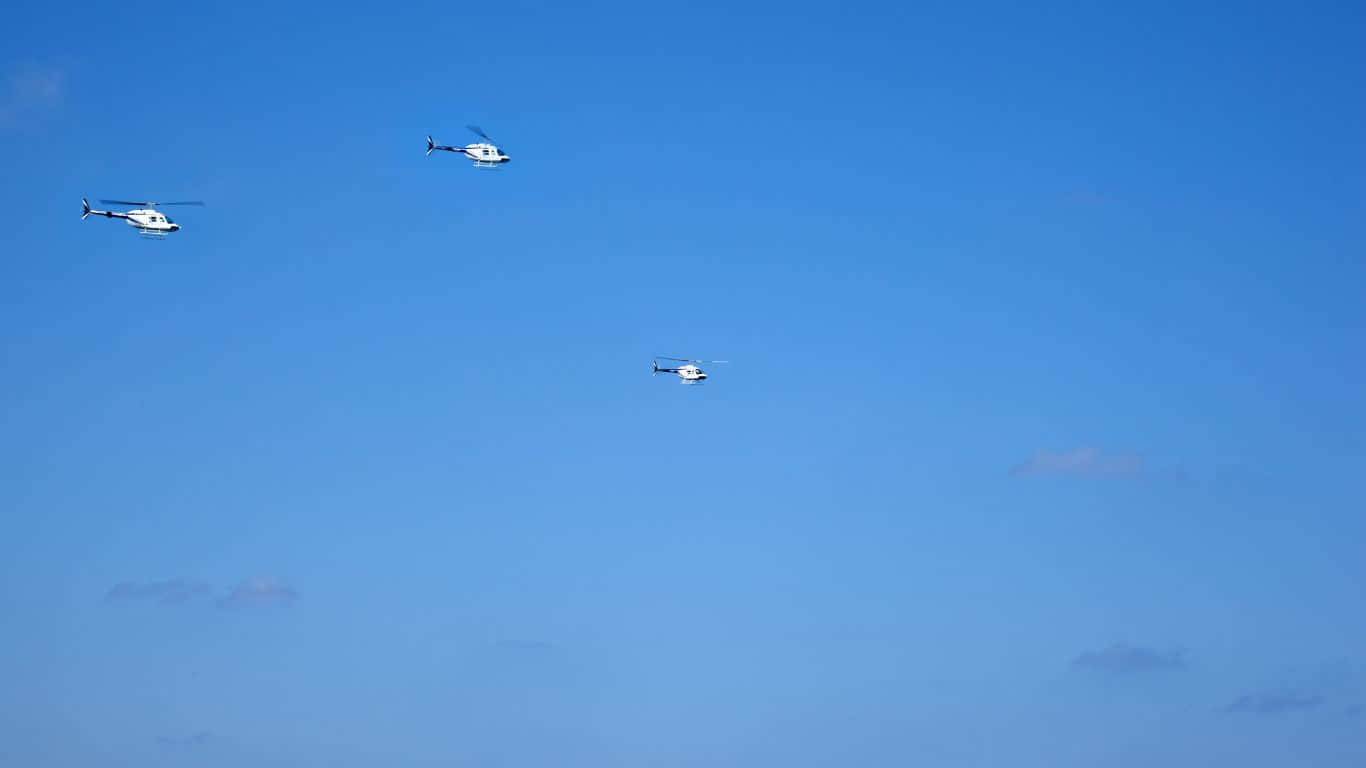 1366x768 Helicopters 桌布 壁紙 — 三架白色直升機編隊飛行，穿越廣闊清澈的藍天，點綴著稀疏的縷縷白雲。