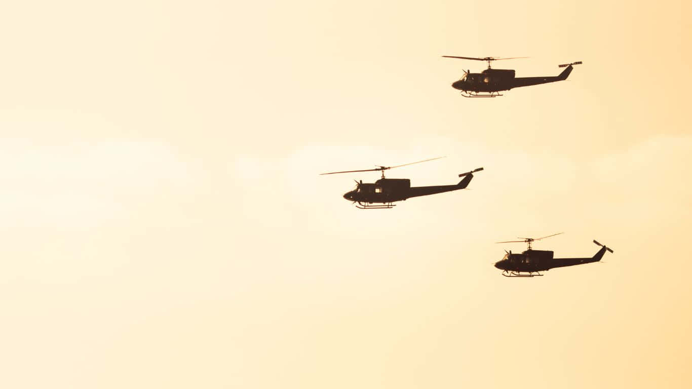 1366x768 Helicopters 桌布 壁紙 — 三架直升機的剪影在溫暖的金色日落天空中編隊飛行。