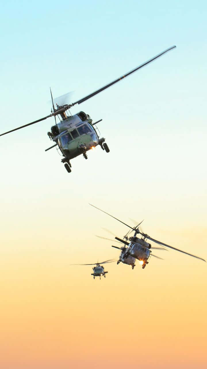 2 桌布 壁紙 — 三架軍用直升機以編隊飛行，背景是帶有溫暖橙色和冷藍色調的漸變日落天空。