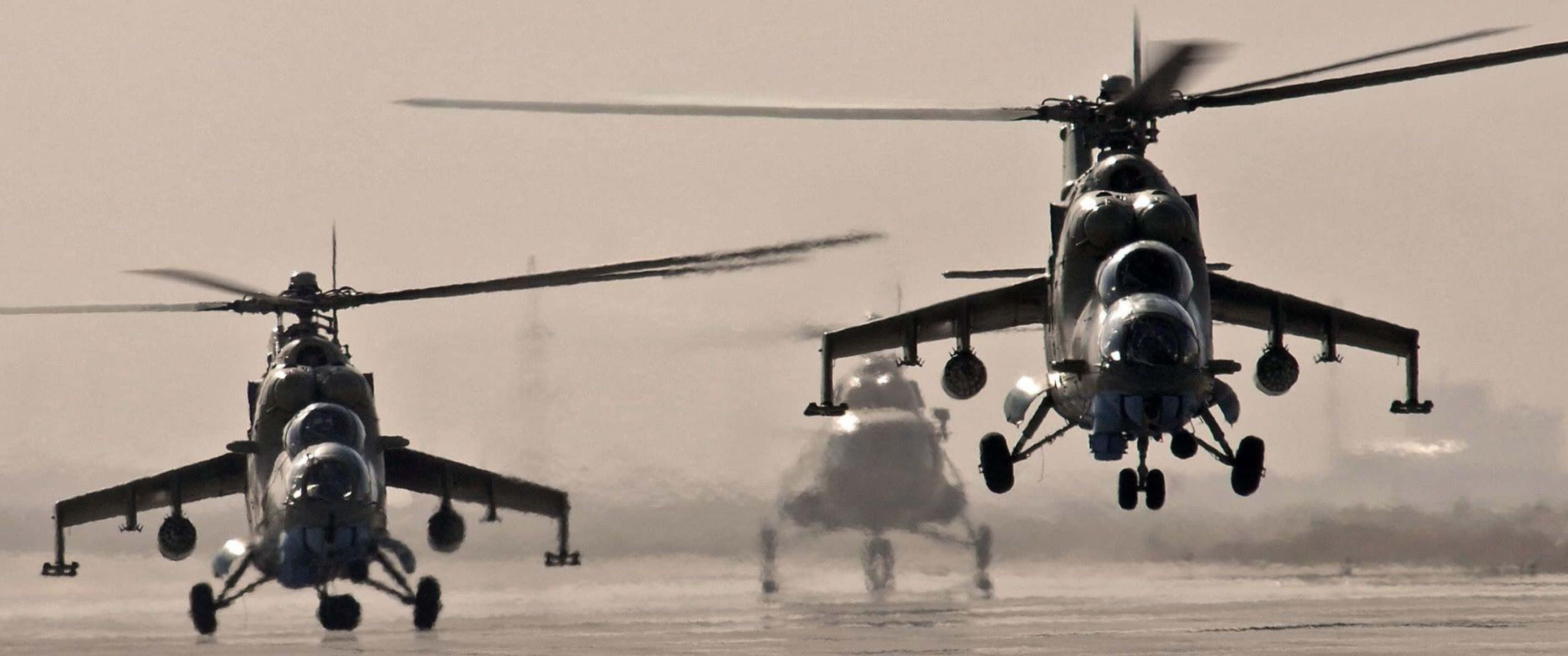 3440x1440p Helicopters 桌布 壁紙 — 三架軍用直升機在塵土飛揚的機場低空盤旋，在朦朧的沙漠環境中揚起沙塵。