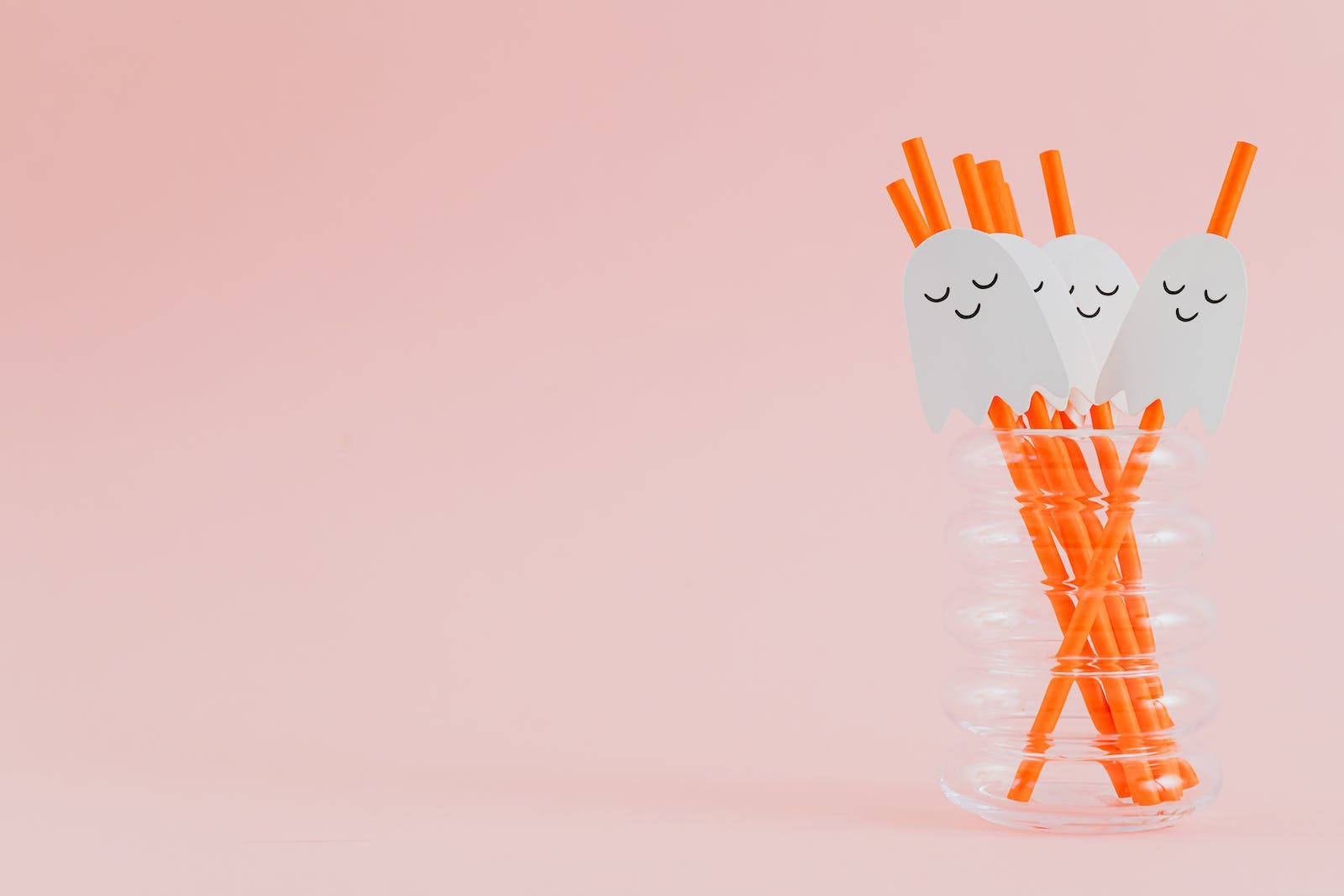 Cute Halloween Desktop 桌布 壁紙 — 三根可愛鬼臉吸管閉著眼睛，從透明螺旋玻璃杯中探出頭來，襯著柔和的粉紅色背景。
