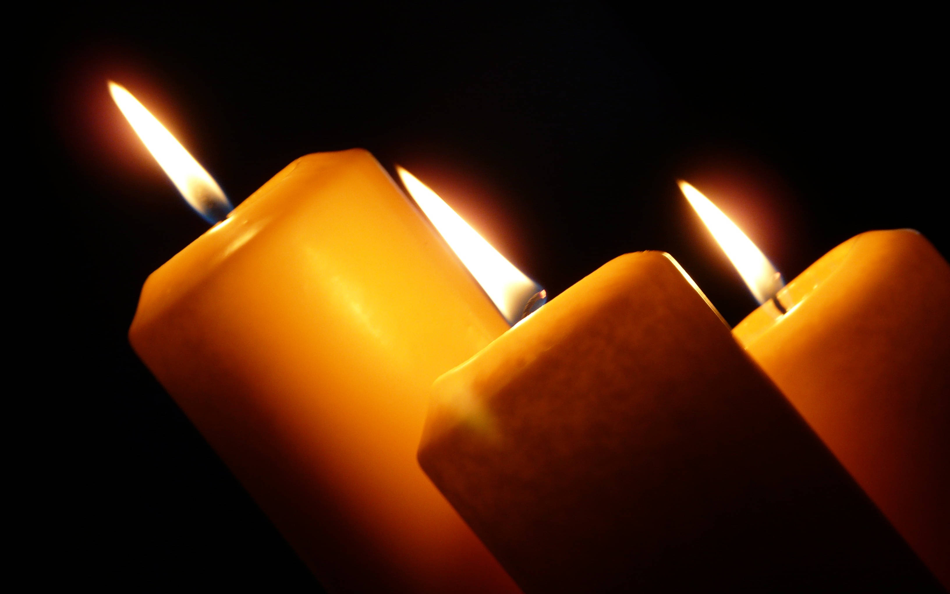 Condolence 桌布 壁紙 — 三根點燃的黃色蠟燭在深黑色背景的特寫鏡頭中溫暖地發光。