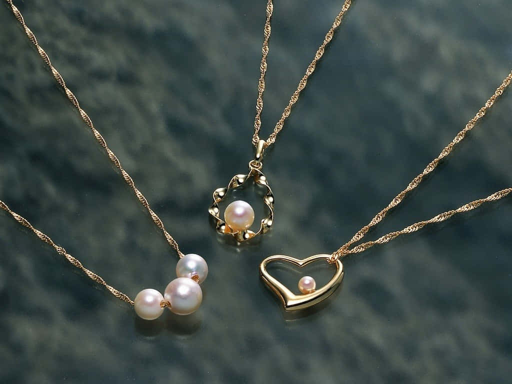 Jewelry Design 桌布 壁紙 — 三條精緻的金色珍珠項鍊放在深色紋理表面上，在柔和燈光下散發柔和光澤。