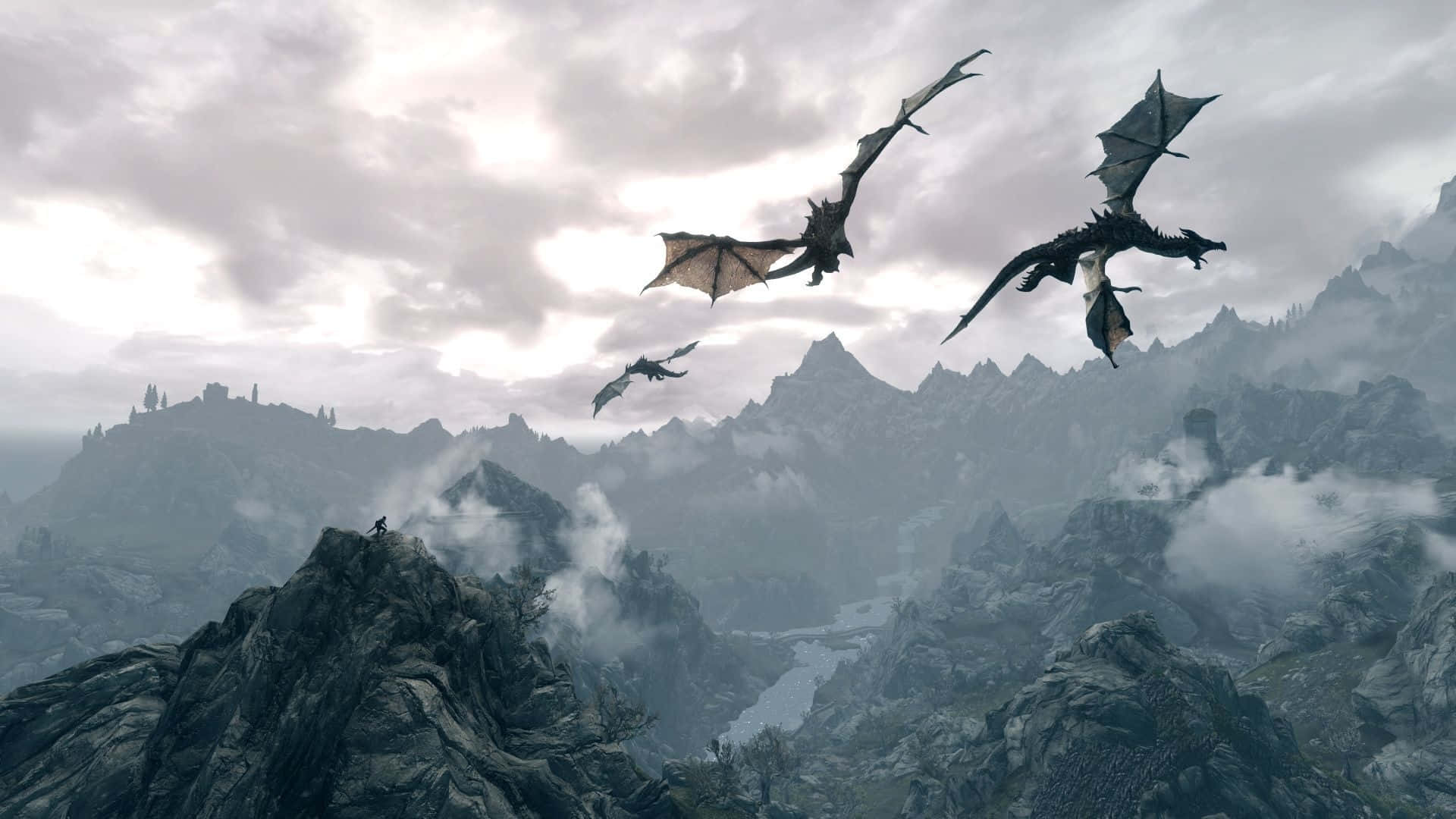 Skyrim Landscapes 桌布 壁紙 — 三條龍在霧氣繚繞的山巒上空翱翔，一個孤獨的身影站在岩石山峰上俯瞰廣闊的山谷。