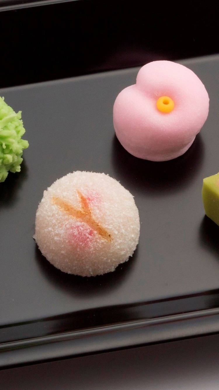 Mochi 桌布 壁紙 — 三款精緻的日本麻糬甜點，配上糖粉和食用花，放在時尚的黑色托盤上。